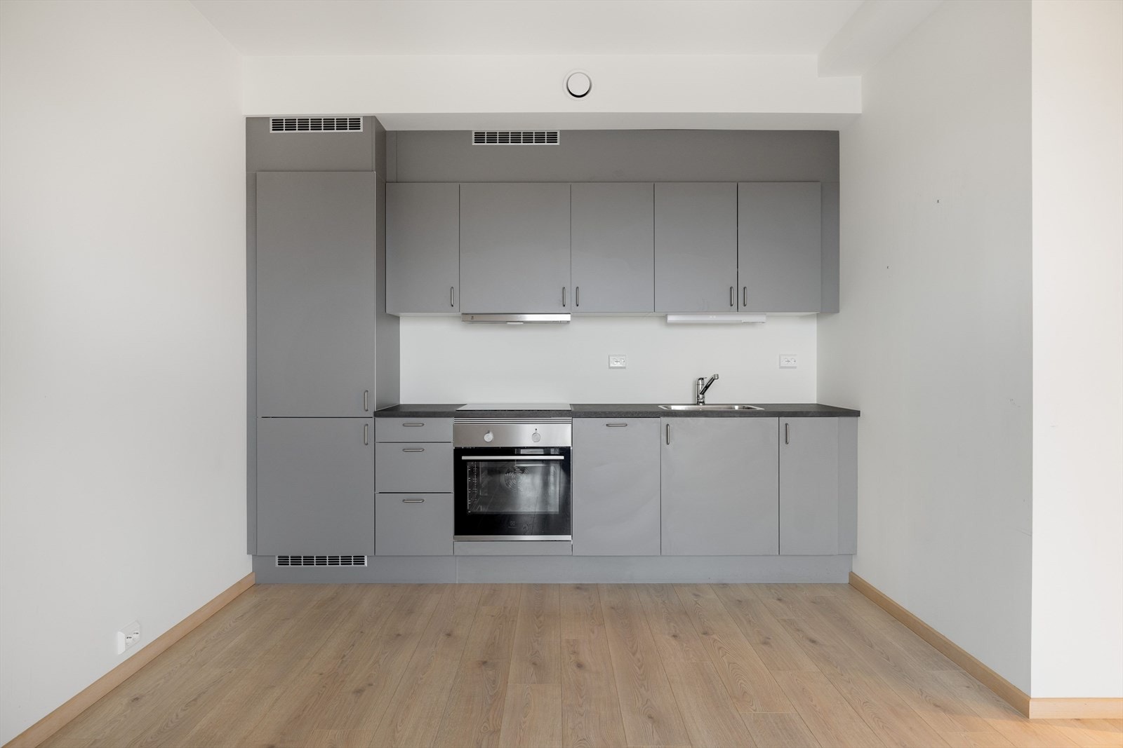 Åpen stue- og kjøkkenløsning med pen og moderne kjøkkeninnredning fra HTH og består av over- og underskap med grå, glatte fronter og laminert benkeplate. Galleribilde