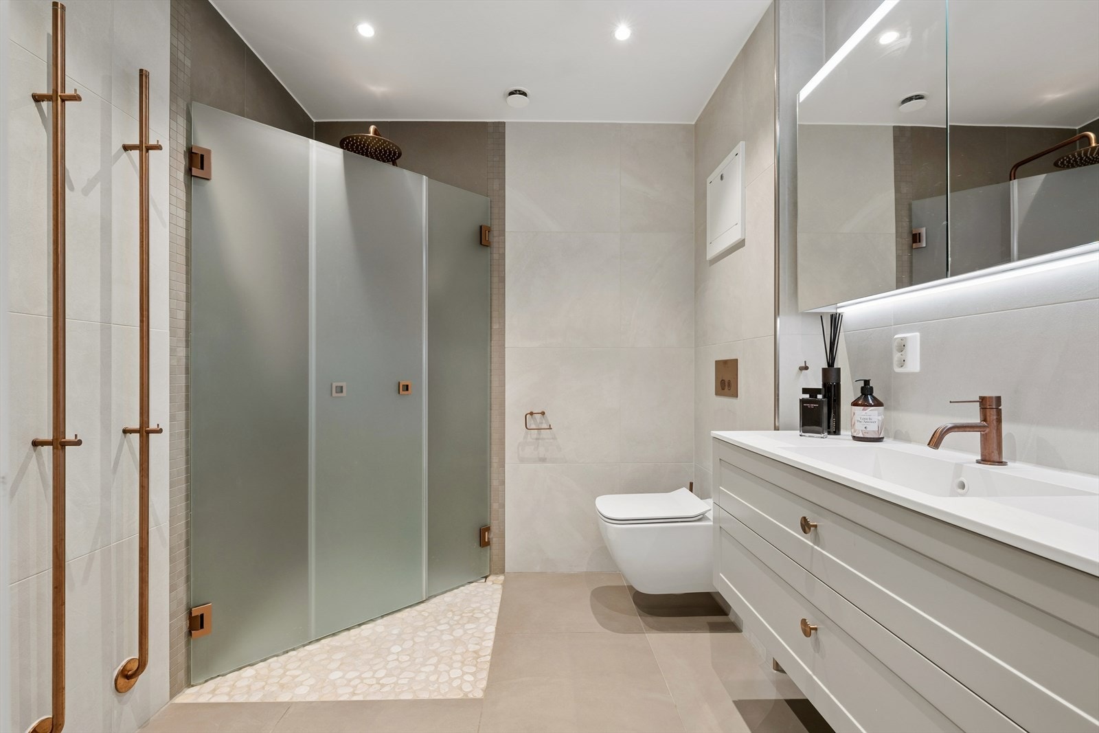 Baderommet har flislagte vegger og malt himling med innfelte downlights. Rommet varmes opp ved bruk av elektriske varmekabler. Galleribilde