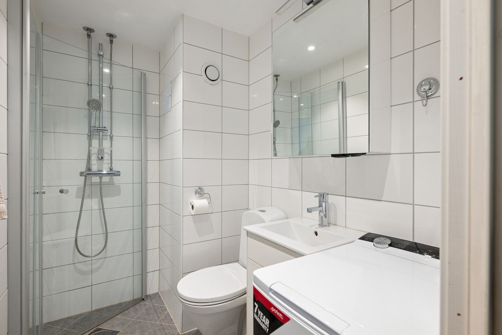 Rommet er utstyrt med en baderomsinnredning med nedfelt servant, toalett og et dusjhjørne med dusjvegger. Det er også opplegg for vaskemaskin på badet. Ventilasjonen er naturlig via en lufteluke i veggen. Galleribilde