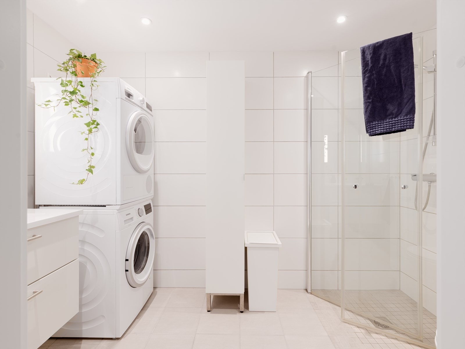 Pent flislagt bad med praktisk dusjhjørne, servant med innredning, klosett og opplegg for vaskemaskin og tørketrommel. Galleribilde