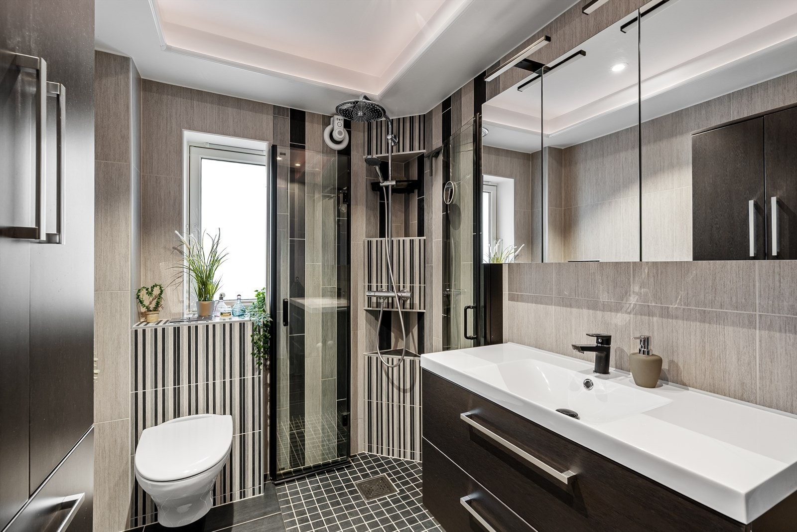 Badet ligger i tilknytning til gangen og er helfliset. Det er innredet med servant, dusj med glassdører, vegghengt toalett med skjult sisterne samt nisje med opplegg for vaskemaskin og tørketrommel. Galleribilde