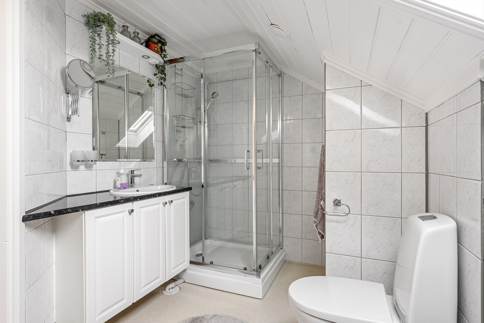 Badet har fliser på veggene og er innredet med toalett, dusjkabinett og servant. Galleribilde