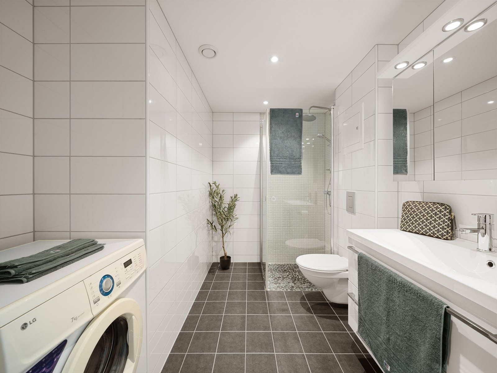 Pent helfliset bad innredet med baderomsinnredning med servant, vegghengt toalett, dusj og opplegg for vaskemaskin. Galleribilde