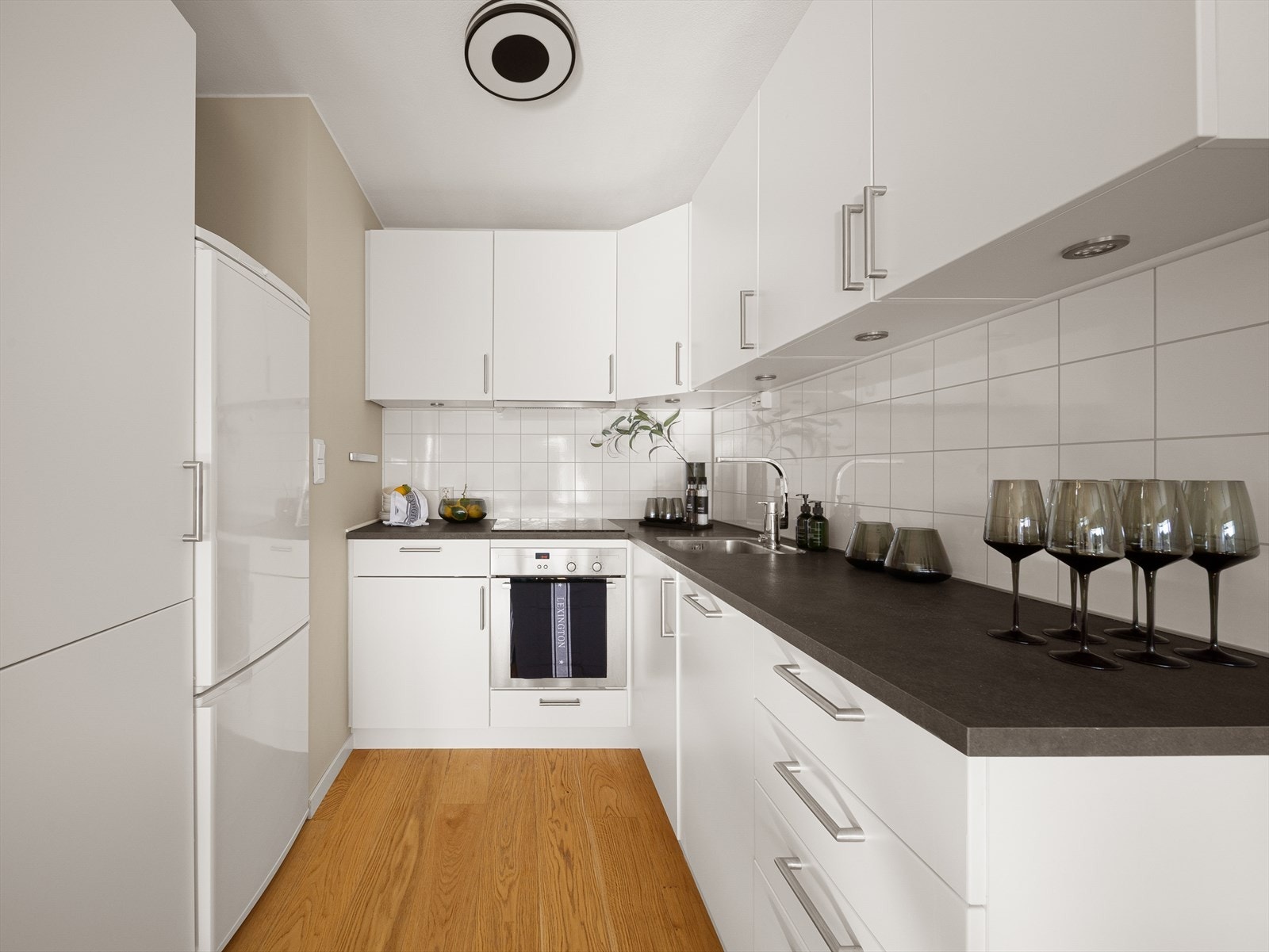 Pent kjøkken med slette, hvite fronter og benkeplate av laminat. Galleribilde