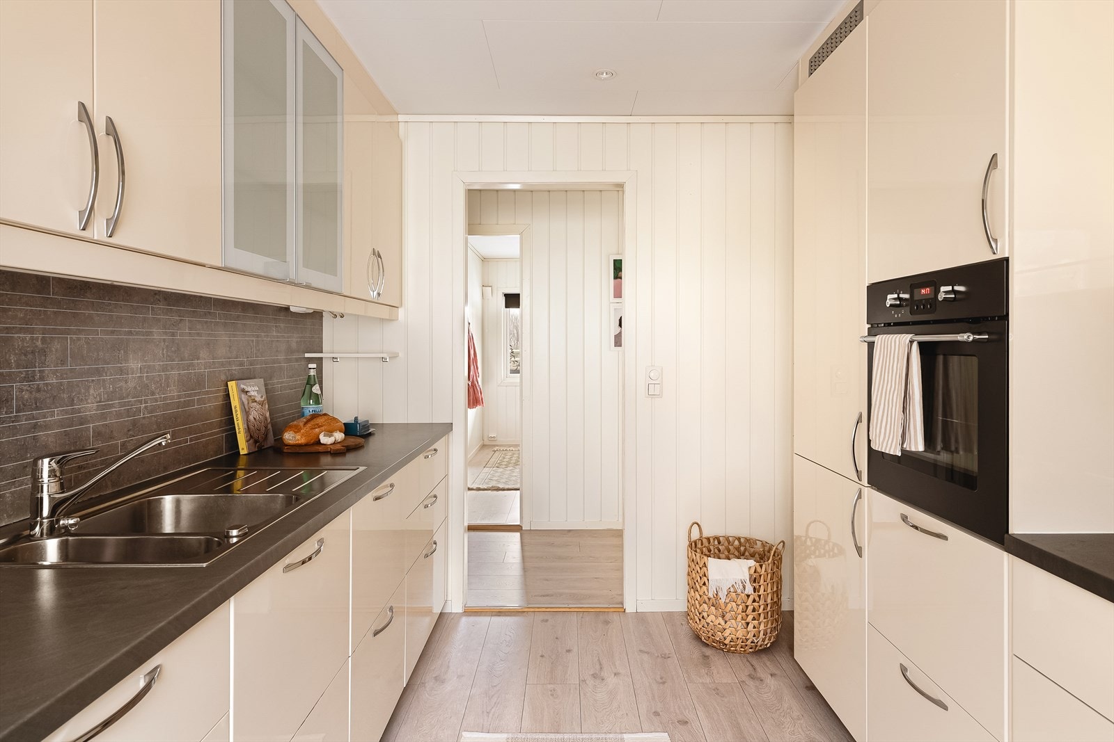 Innredningen er fra IKEA, med slette høyglansfronter og takhøye skap som gir rikelig med oppbevaringsplass. To overskap med glassfronter gir et stilrent uttrykk. Laminat benkeplate med stål vaskekum, ventilator og kitchen boards over benkeplate. Galleribilde