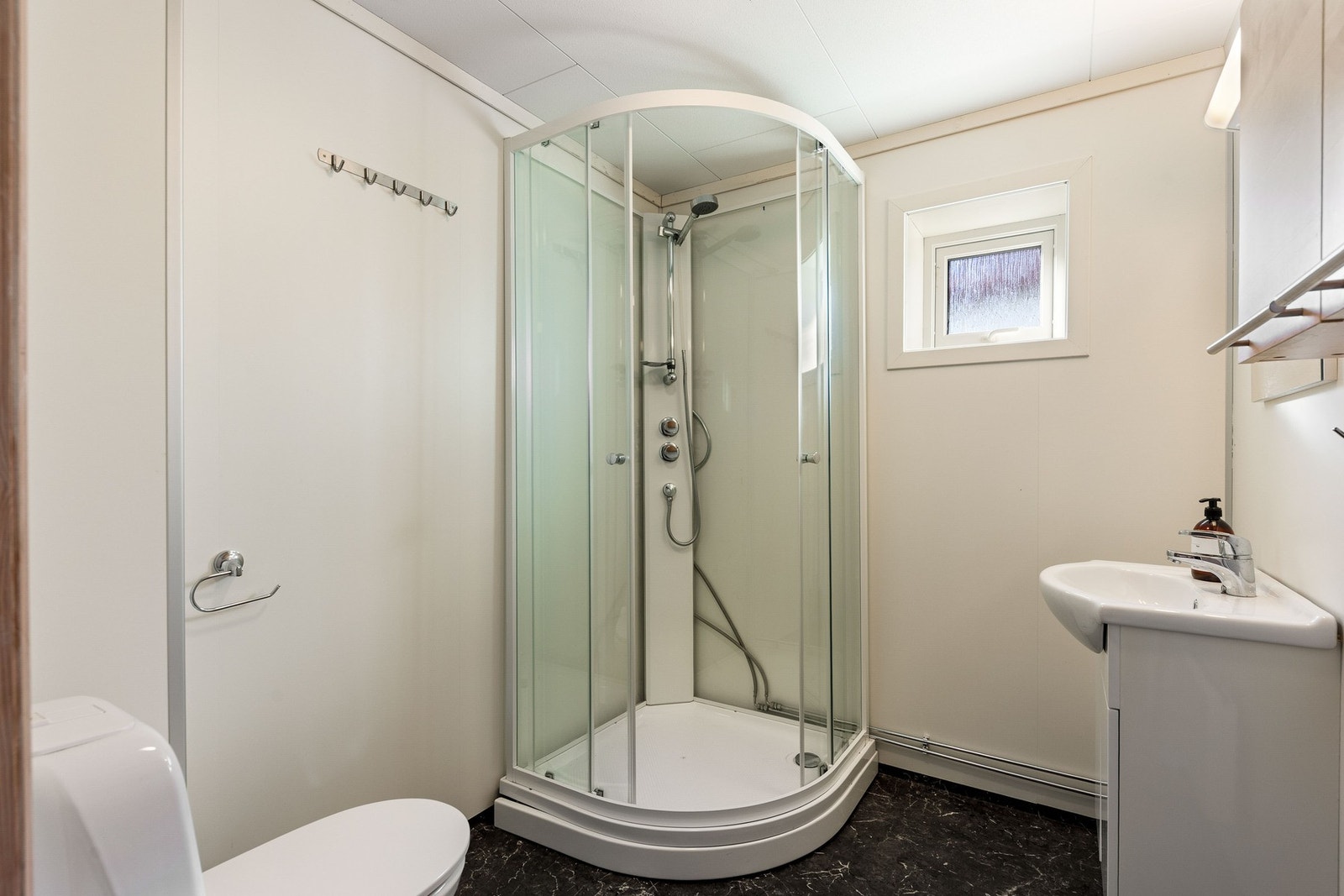 Bad med dusjkabinett, toalett og innredning med vask. Galleribilde