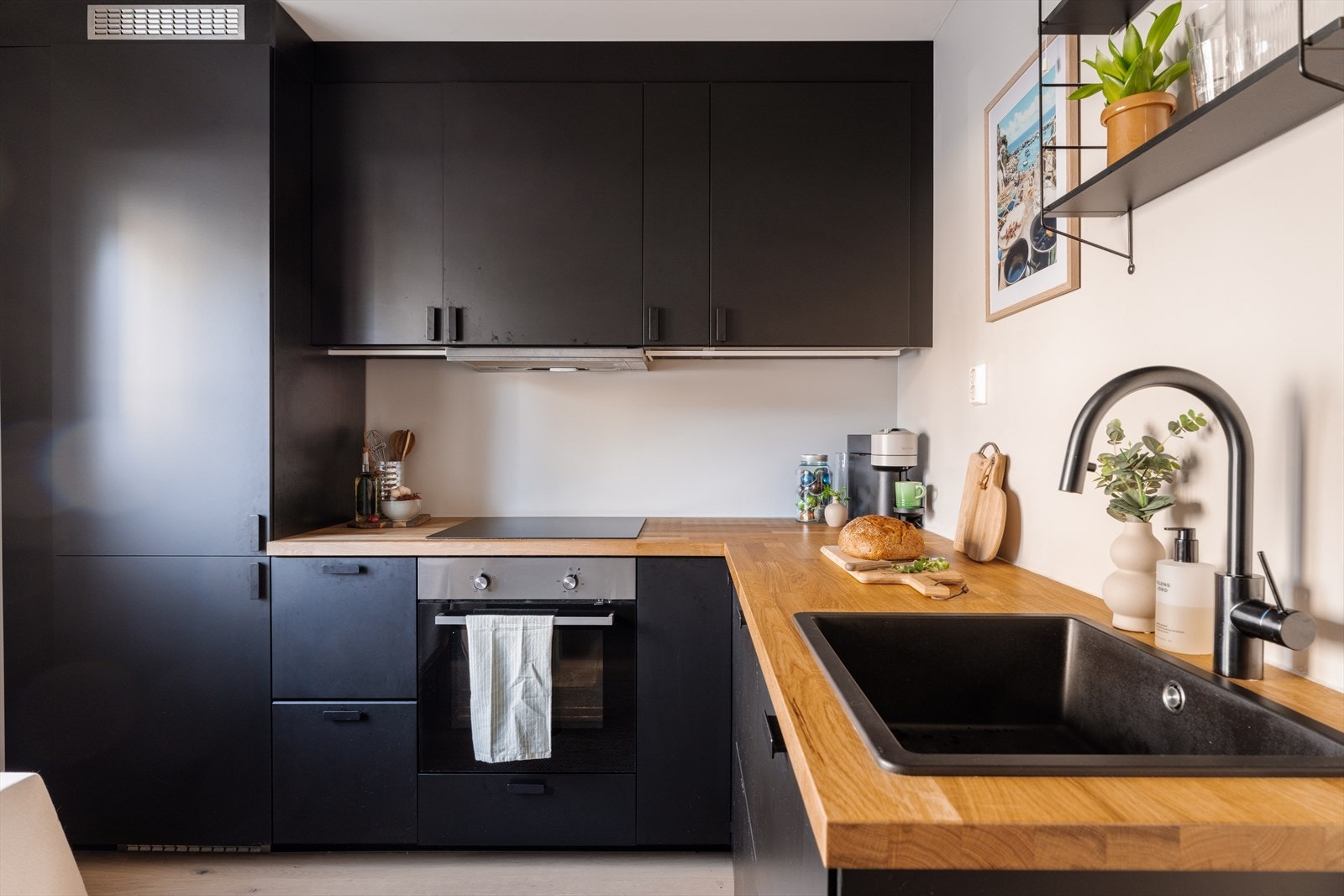 Lekkert kjøkken med sorte, glatte fronter og benkeplate i tre. Plassen er godt utnyttet med god skap- og benkeplass. Galleribilde