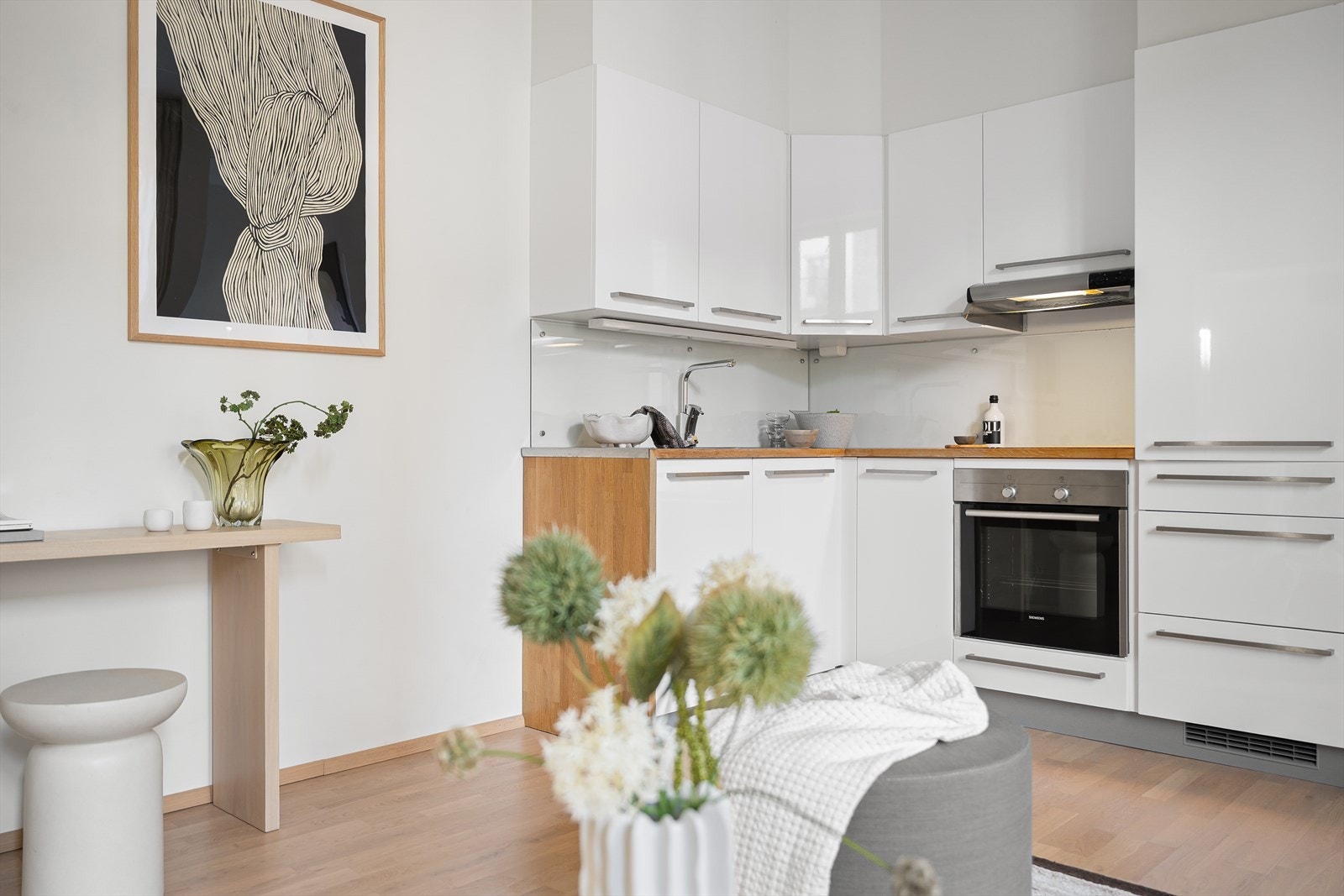Lyst kjøkken fra Kvik med hvite glatte fronter, plate på vegg over benkeskap og heltre benkeplate med nedfelt kum i rustfritt stål. Galleribilde