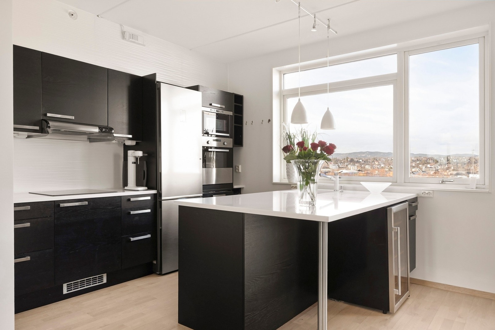 Moderne kjøkkeninnredning med slette fronter, kompositt benkeplate og flislagt vegg over benk. Galleribilde