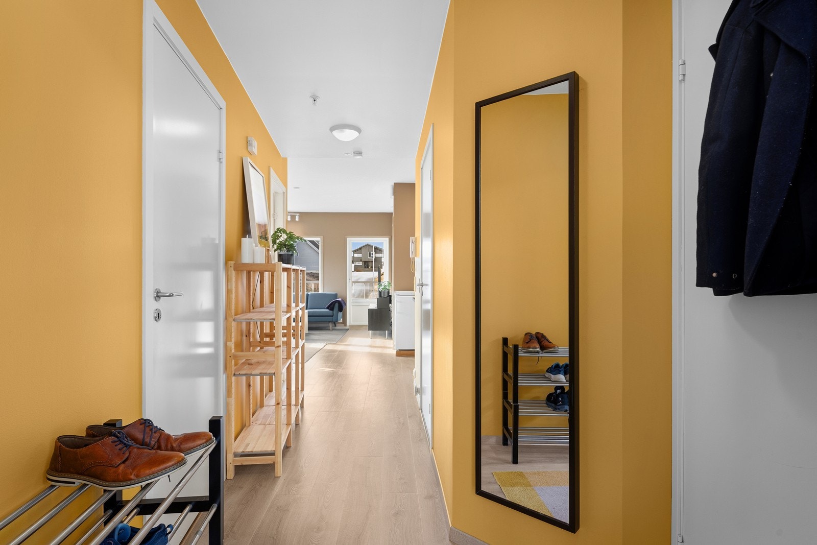 Lyse laminatgulv strekker seg gjennom gangen og gir en naturlig overgang inn til stuen. Galleribilde