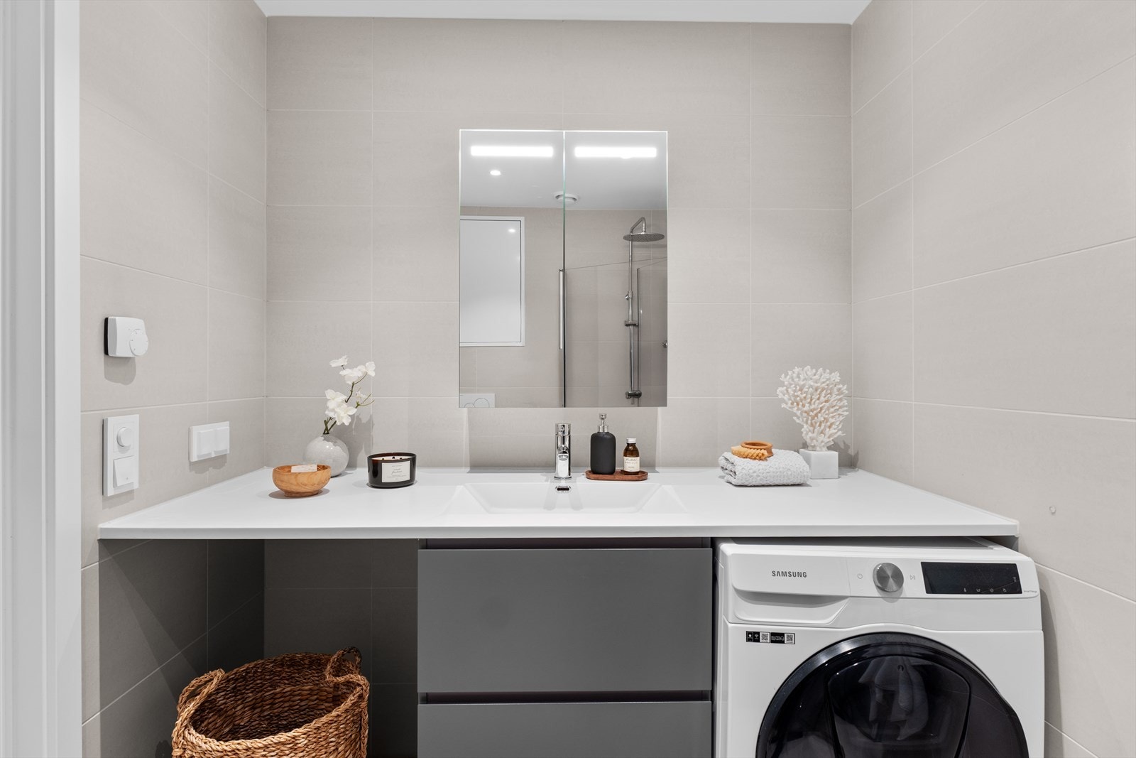 Badet er innredet med heldekkende servant på underskap som gir praktisk oppbevaring, samt speil med belysning.
Videre er rommet utstyrt med vegghengt toalett og en dusjsone med dusjvegger i herdet glass. Det er også opplegg for vaskemaskin. Galleribilde