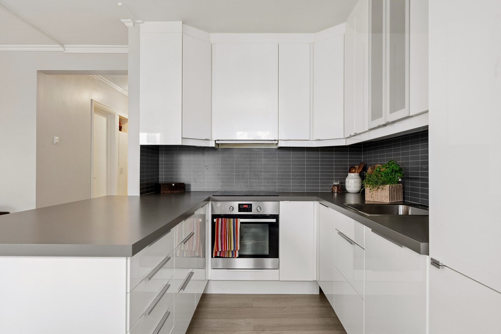 Kjøkkenet har hvite glatte fronter, benkeplate av laminat og plater over benk. Galleribilde