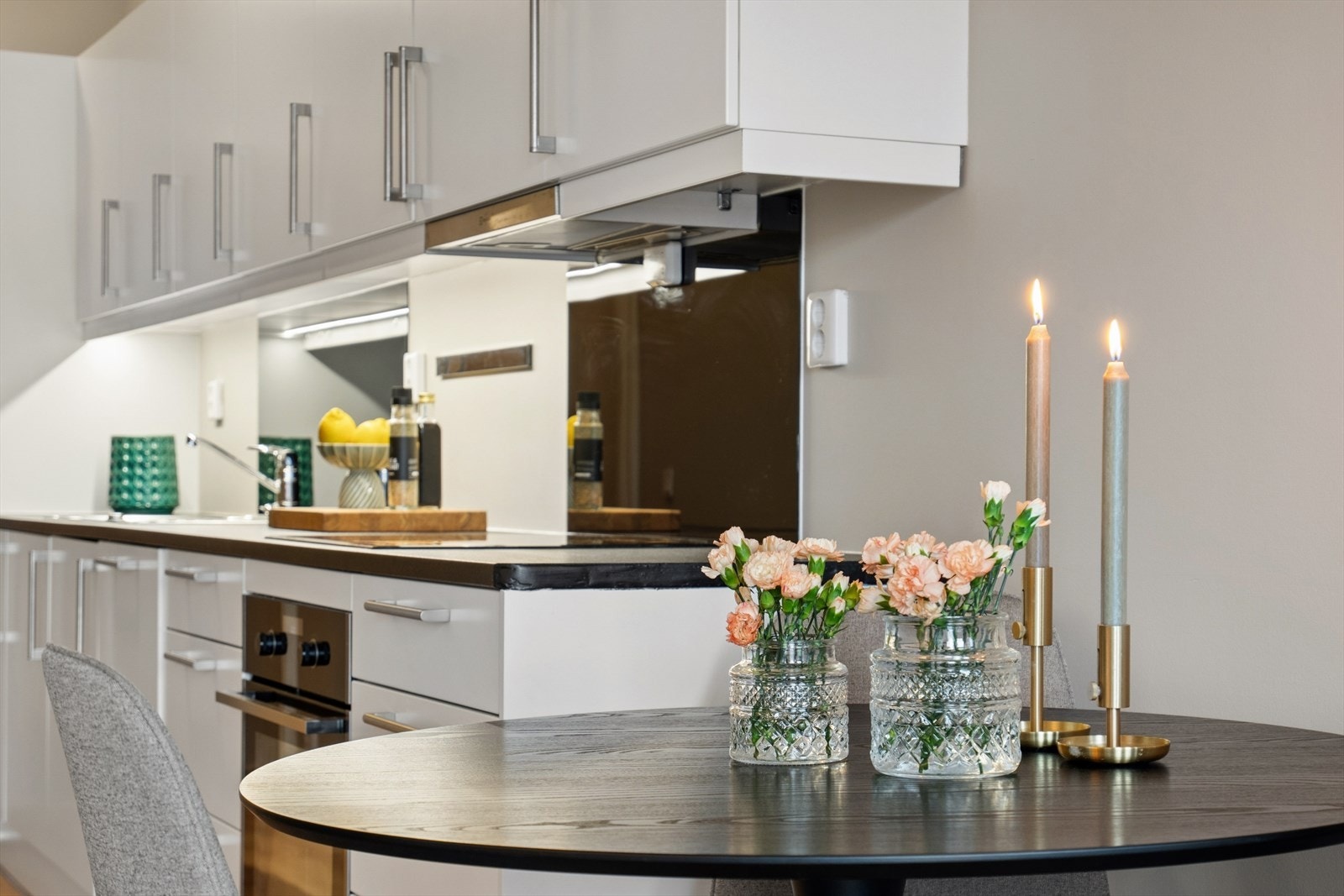 Innredningen har glatte hvite fronter, benkeplate i laminat med nedfelt kjøkkenvask i stål og backsplash på vegg over kokesone og vask Galleribilde