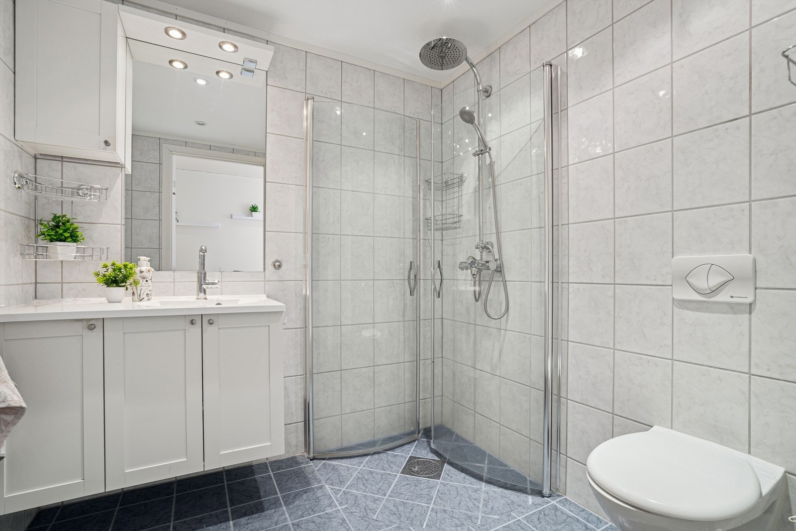 Badet er flislagt på vegger og gulv, utstyrt med elektriske varmekabler i gulvet. Innredningen har nedfelt servant, veggmontert toalett, dusjvegger/hjørne og opplegg for vaskemaskin Galleribilde