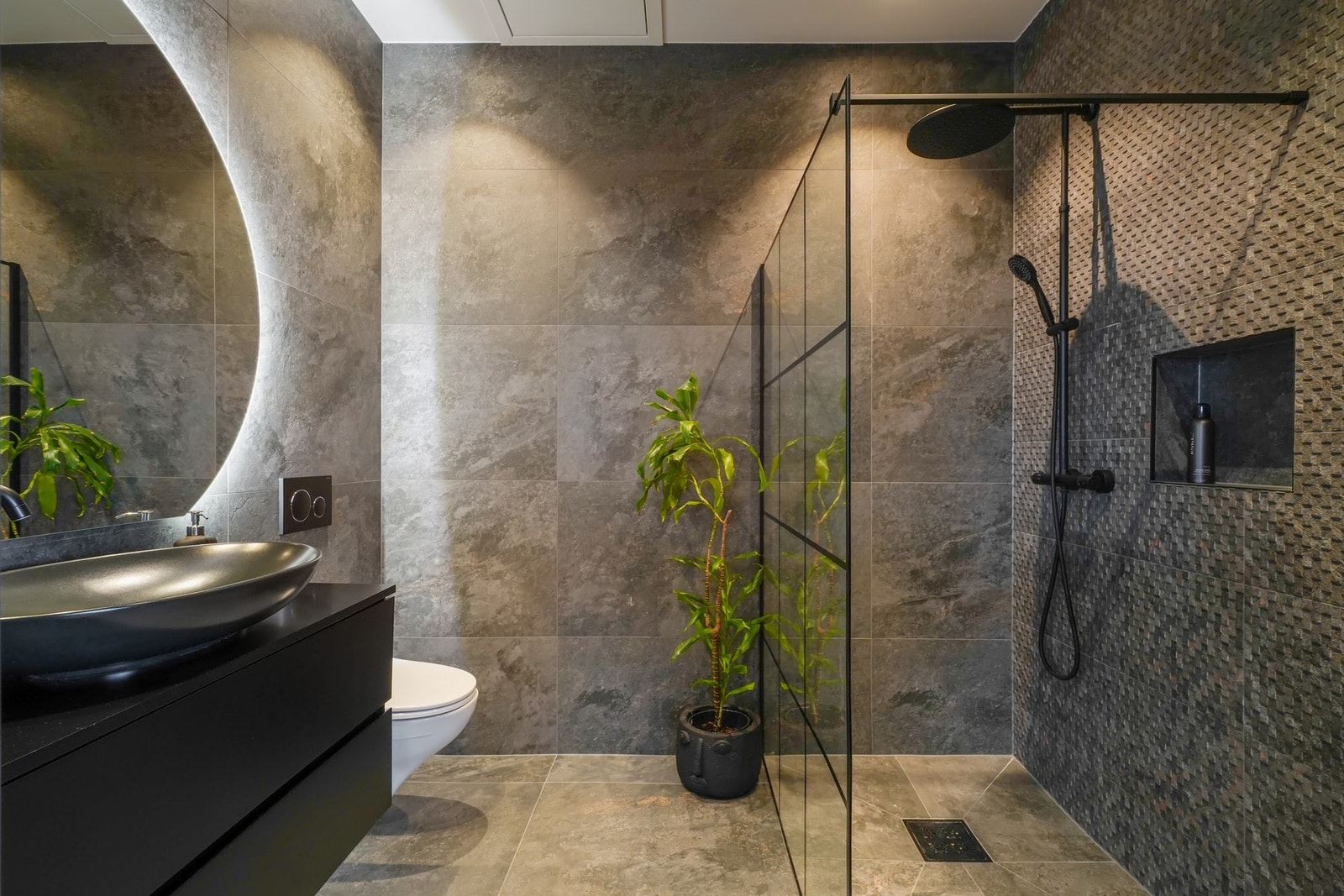 Innredet med vegghengt toalett, morderne innredning med overliggende design servant og rundt speil med belysning bak. Galleribilde