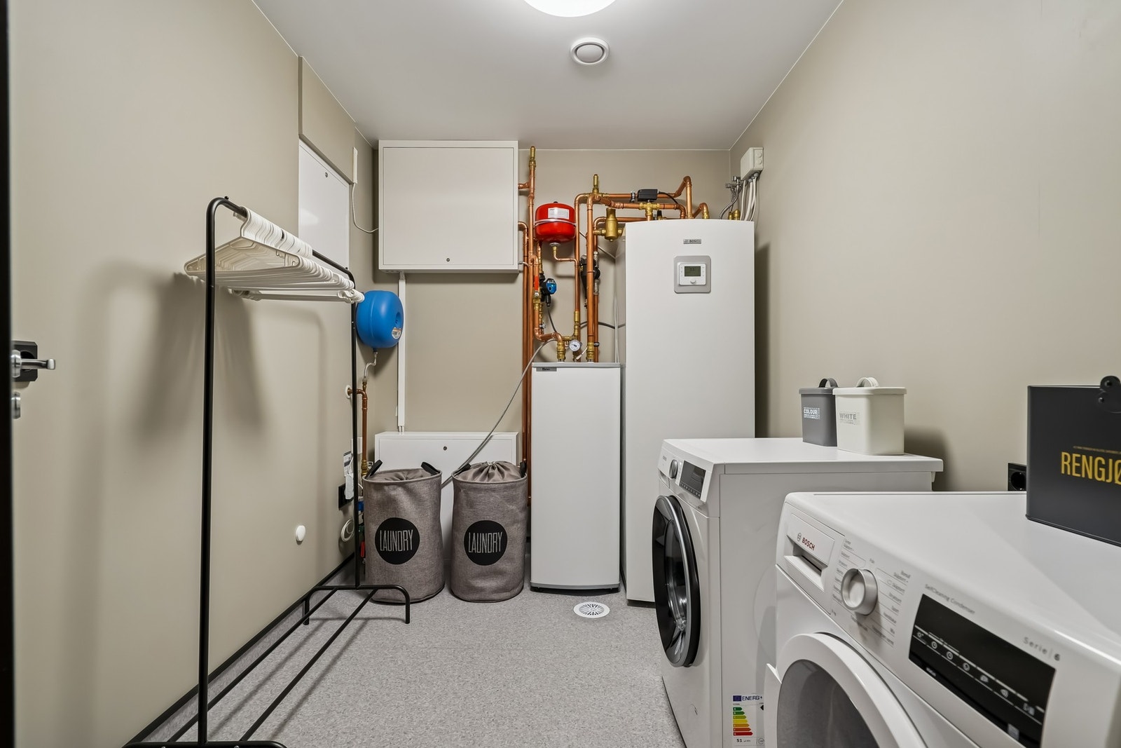 Et praktisk vaskerom med vinylbelegg på gulvet og malte vegger. Innredet med opplegg for vaskemaskin og tørketrommel. Galleribilde