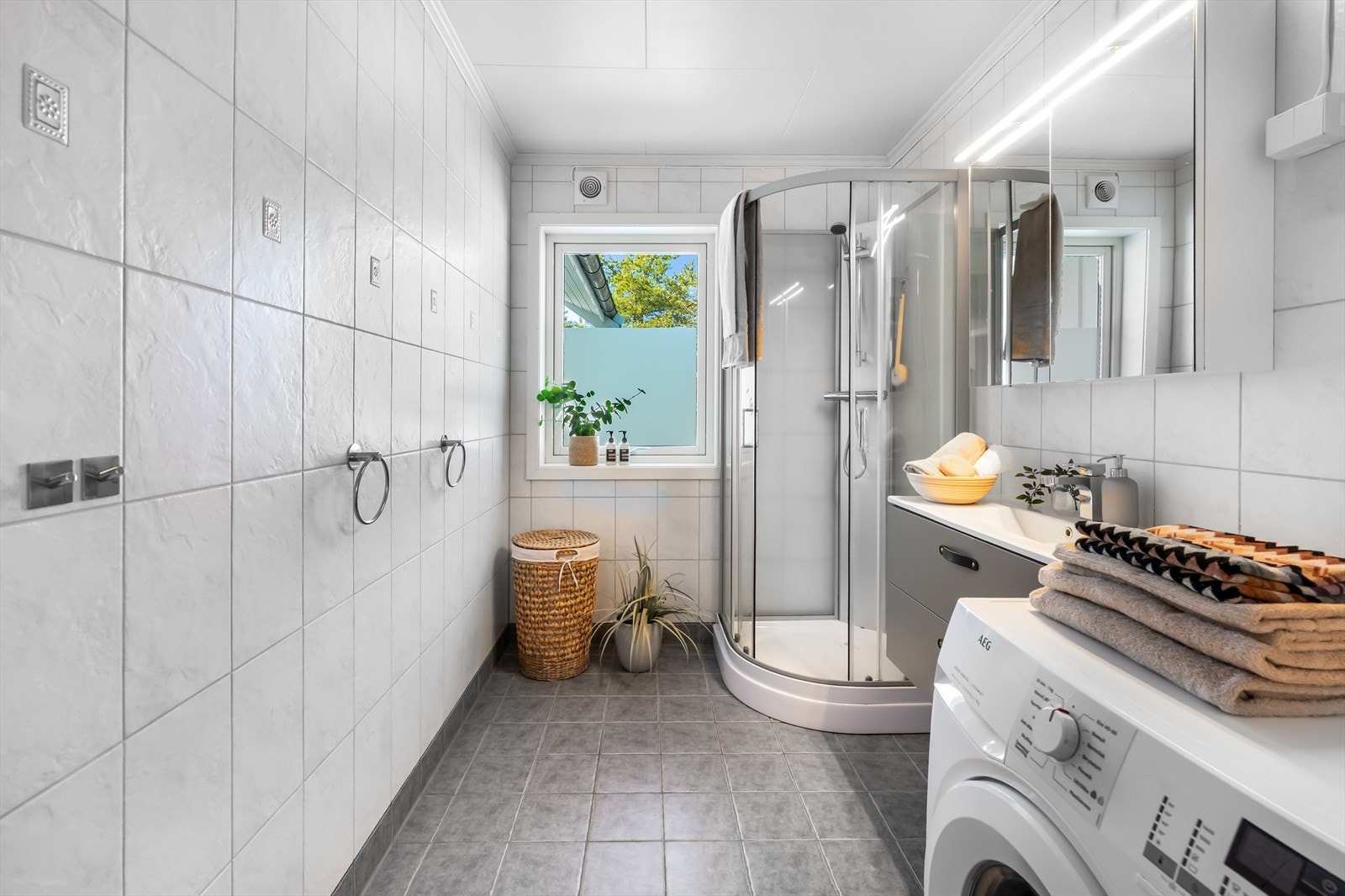 Helfliset baderom i 1. etasje innredet med dusjkabinett, servant med innredning, speil og belysning. Opplegg for vaskemaskin. Det er elektriske varmekabler i gulvet for en behagelig temperatur. Galleribilde