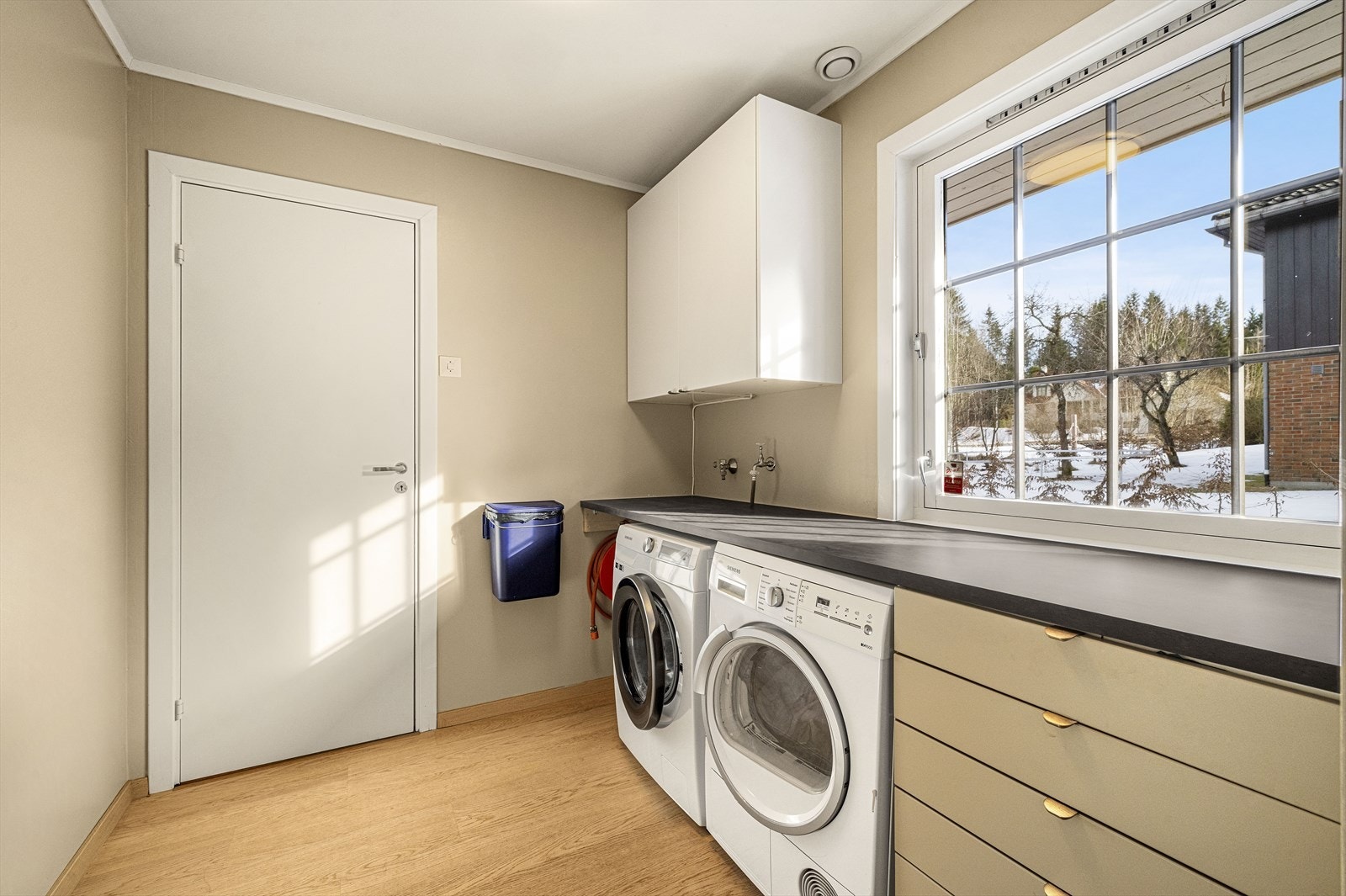 Praktisk vaskerom på innsiden av kjøkkenet, med opplegg for vaskemaskin og tørketrommel under innredning Galleribilde