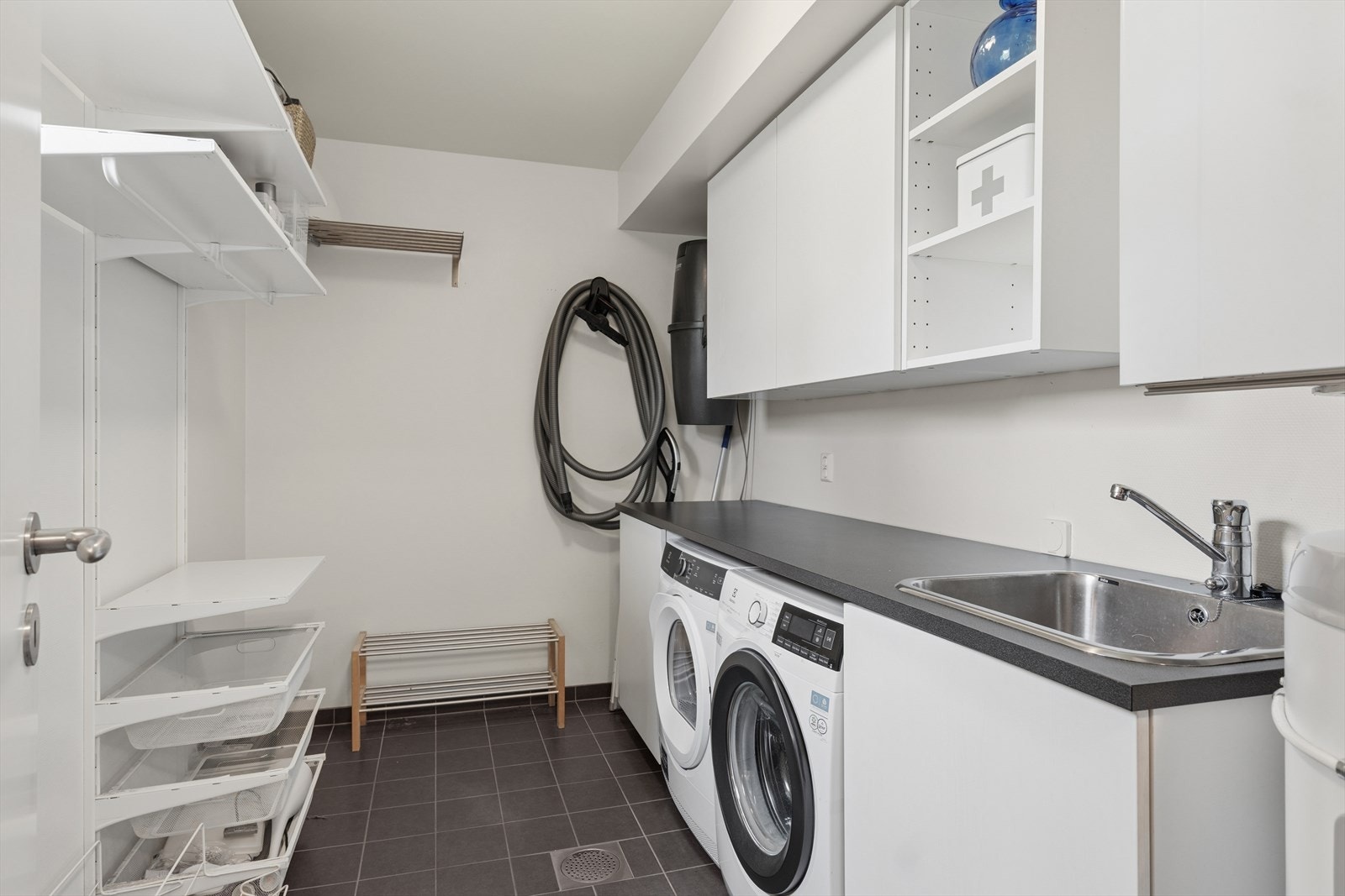 Vaskerom med opplegg til vaskemskin og tørketrommel, sentralstøvstøvsuger og praktisk oppbevaring for å holde orden og ryddighet i gang og hall. Galleribilde