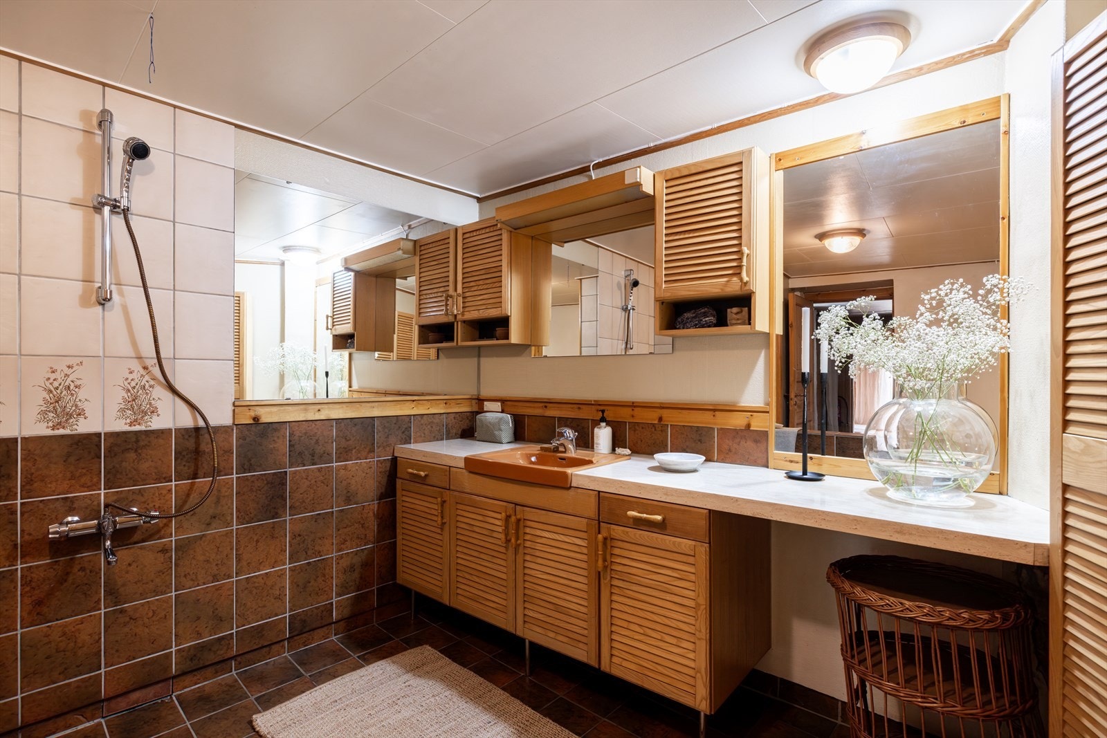 Stort baderom med dusjhjørne, servant i nedfelt innredning og toalett. Flislagte gulv og vegger gir et stilrent uttrykk, mens himlingen er malt. Galleribilde