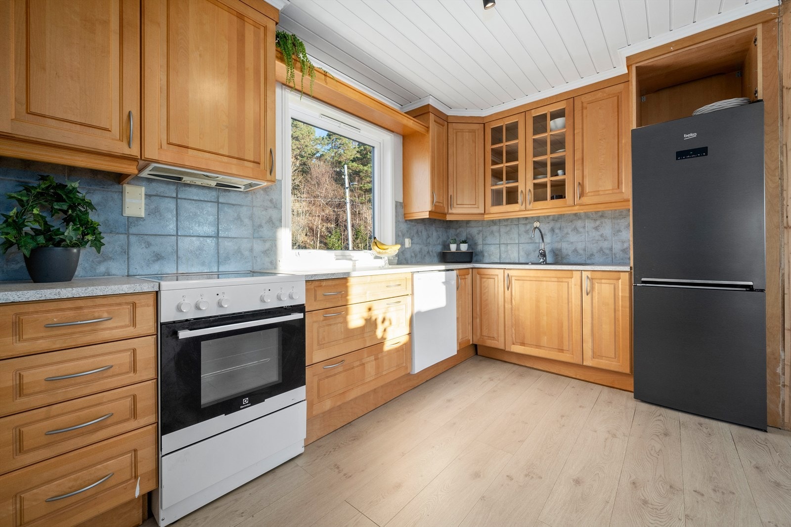 L-formet kjøkkeninnredning med laminat benkeplate. Frittstående komfyr og kjøleskap, samt innfelt oppvaskmaskin medfølger. Galleribilde