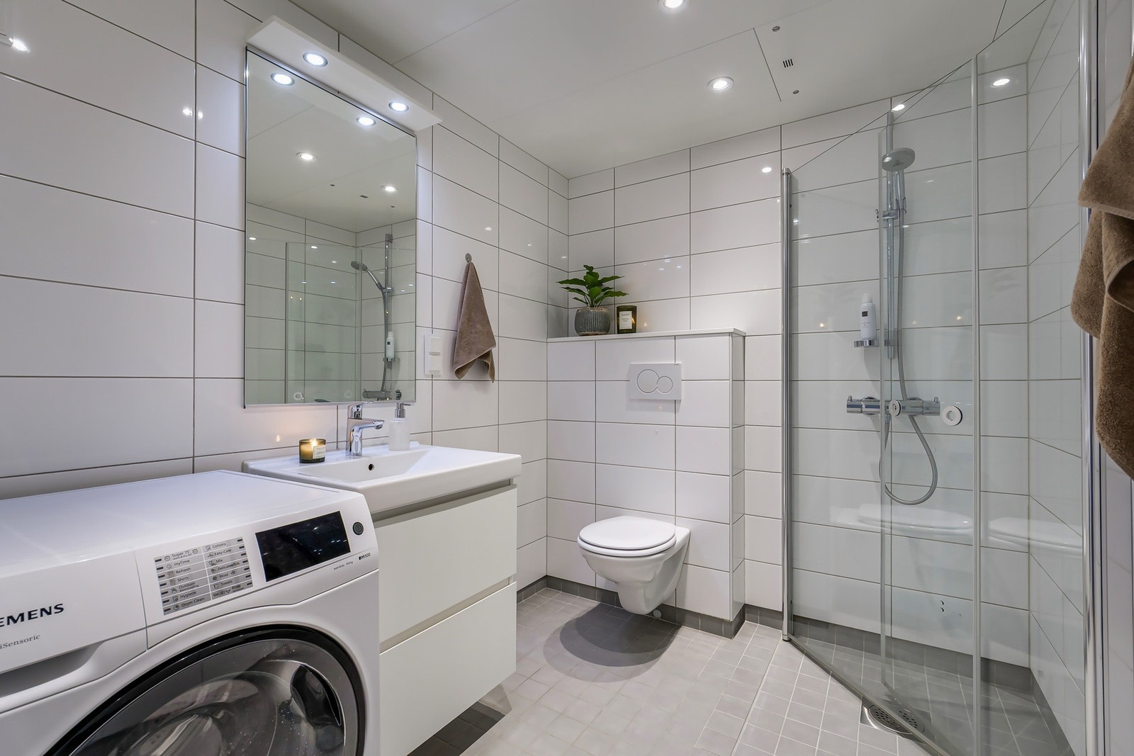 Tidsriktig baderom med vegghengt toalett, servant nedfelt i innredning, speilskap og dusjhjørne med svingbare glassdører. Galleribilde