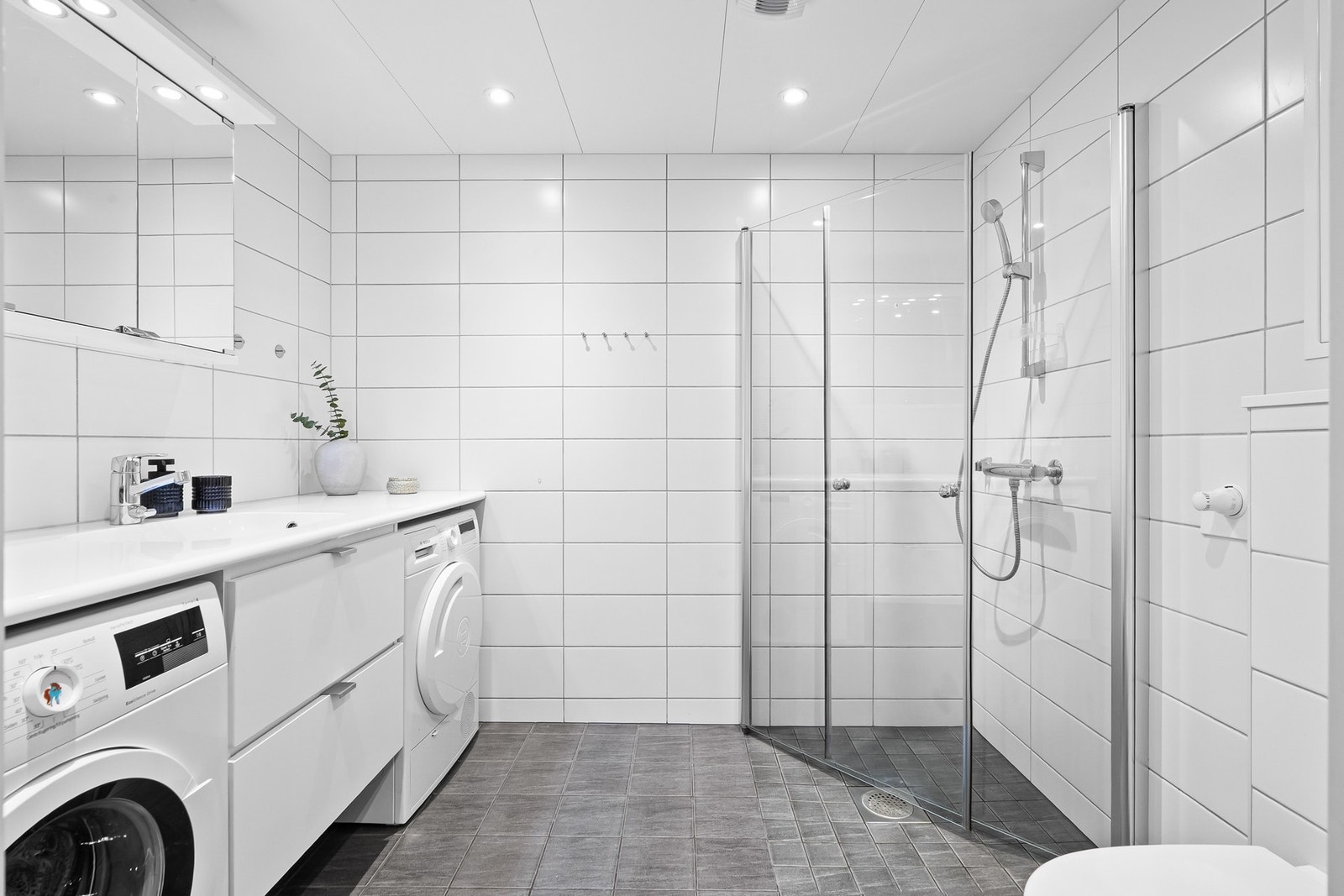 Stilrent baderom med plass til vaskemaskin og tørketrommel under vegg til vegg benkeplate Galleribilde