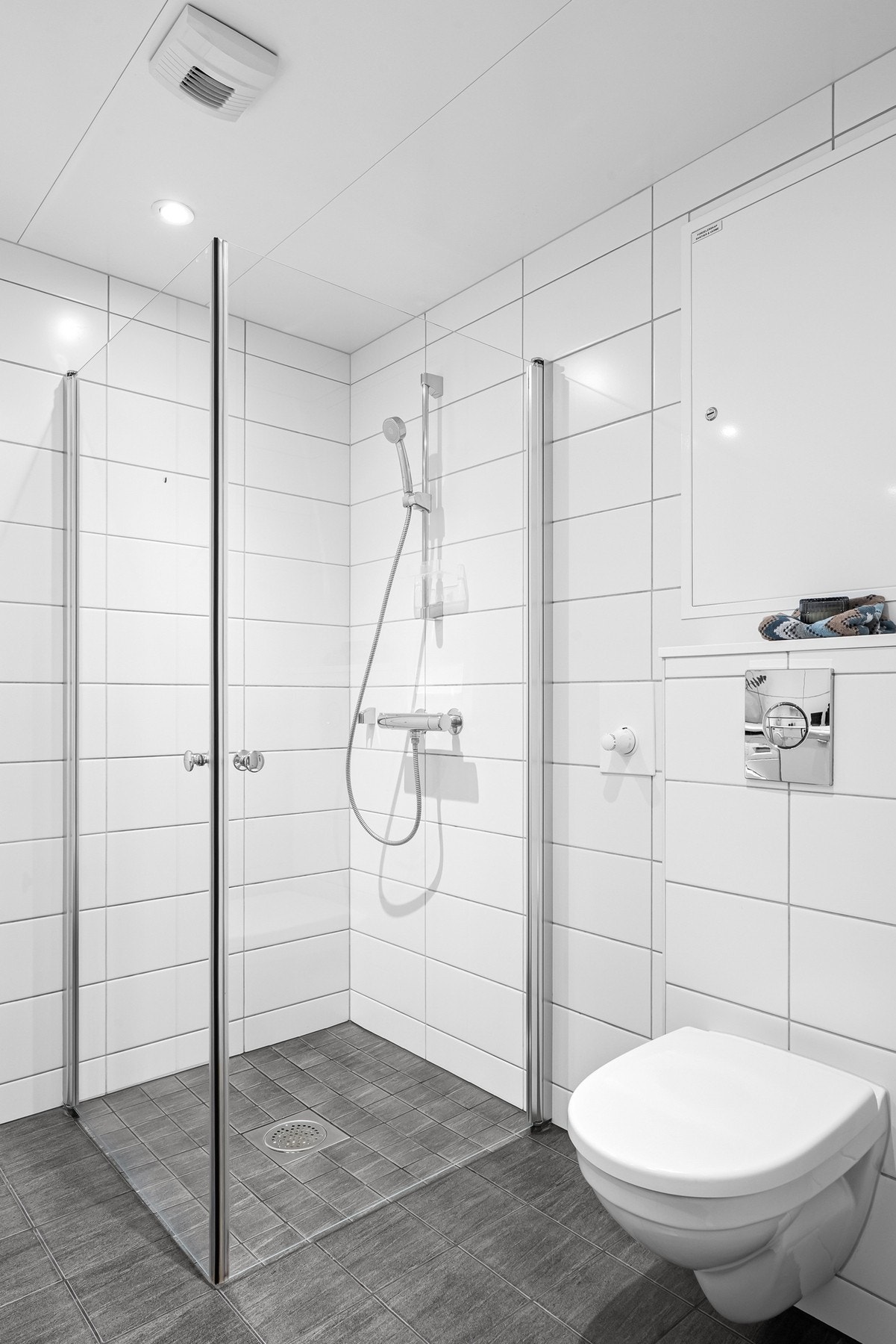 Dusjhjørne med rette foldbare glassdører. Det er varme i gulv og downlights i himling Galleribilde