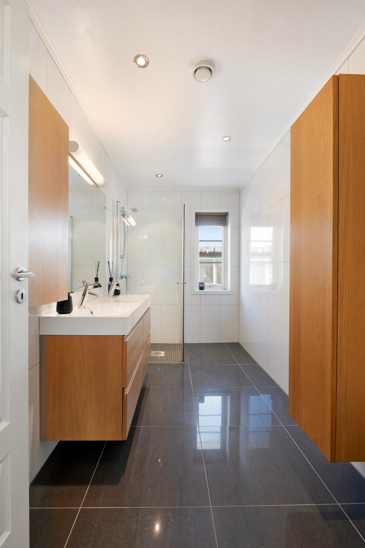 Badet er tidløst flislagt med varmekabler i gulvet og gir deg god oppbevaringsplass i høyskap og servantinnredning Galleribilde