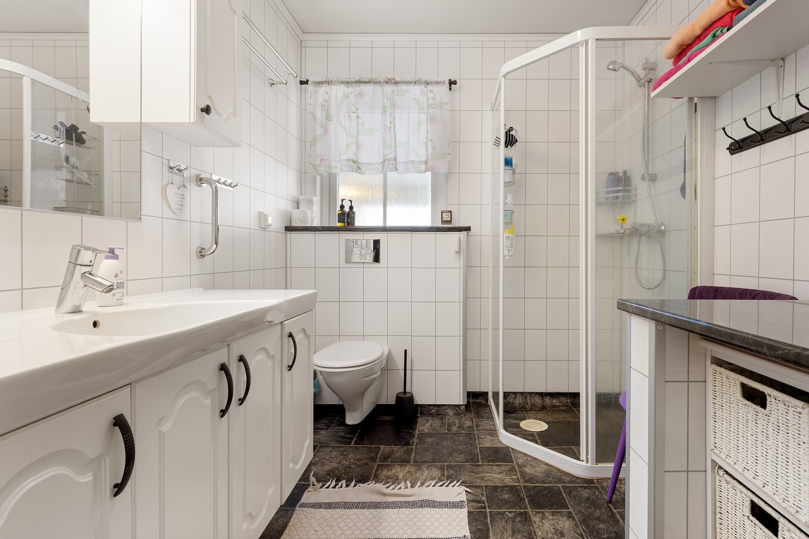 Badet er innredet med baderomsinnredning med servant, veggmontert toalett og dusjhjørne. Galleribilde