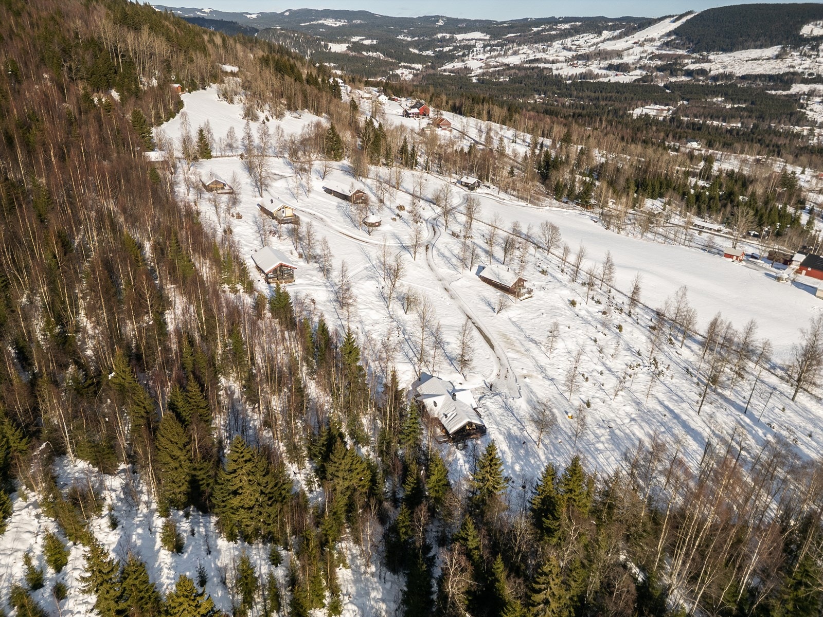 Droneperspektivet viser også den naturskjønne utsikten mot Hurdal Skisenter og Hurdalsjøen i det fjerne, samt den overbygde verandaen, bålplassen og uteområdene som skaper perfekte rammer for hytteliv året rundt. Galleribilde