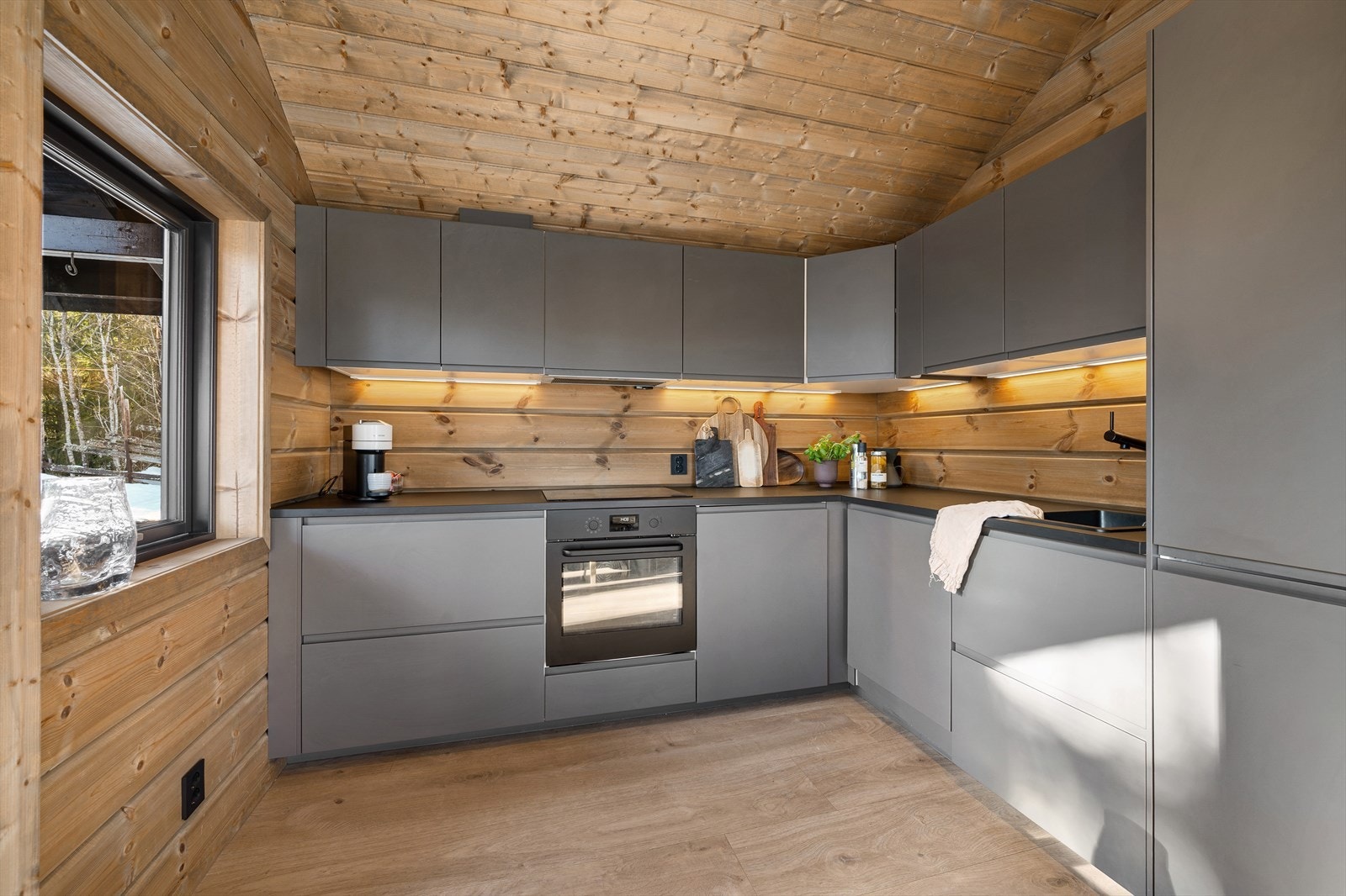 Den robuste laminatbenkeplaten gir gode og romslige arbeidsflater, perfekt for både matlaging og hyggelige måltidsforberedelser. Den mørke komposittvasken kombinert med sort armatur gir et moderne og eksklusivt preg som står flott til de rene linjene. Galleribilde