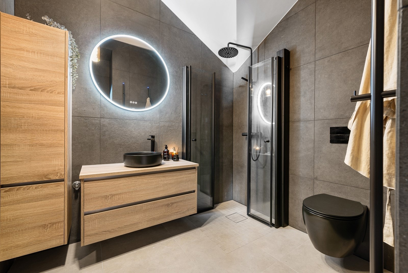 Baderommet fremstår som lekkert, moderne og gjennomført med et stilrent design og høy funksjonalitet. Store 60×60 fliser gir rommet et elegant uttrykk og skaper en følelse av romslighet, mens dusjen med herdet glass og sorte detaljer gir et moderne preg. Galleribilde