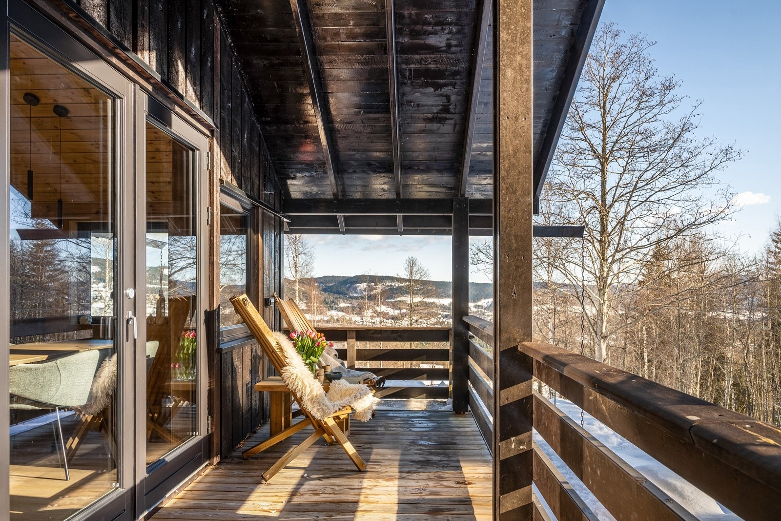 Fra spisestuen og kjøkkenet tar vi turen ut på den romslige, overbygde verandaen som omkranser hytta. Her er det plass til flere sittegrupper, trestoler og grill, og området inviterer til hyggelige måltider ute eller rolige kvelder med utsikt mot naturen. Galleribilde