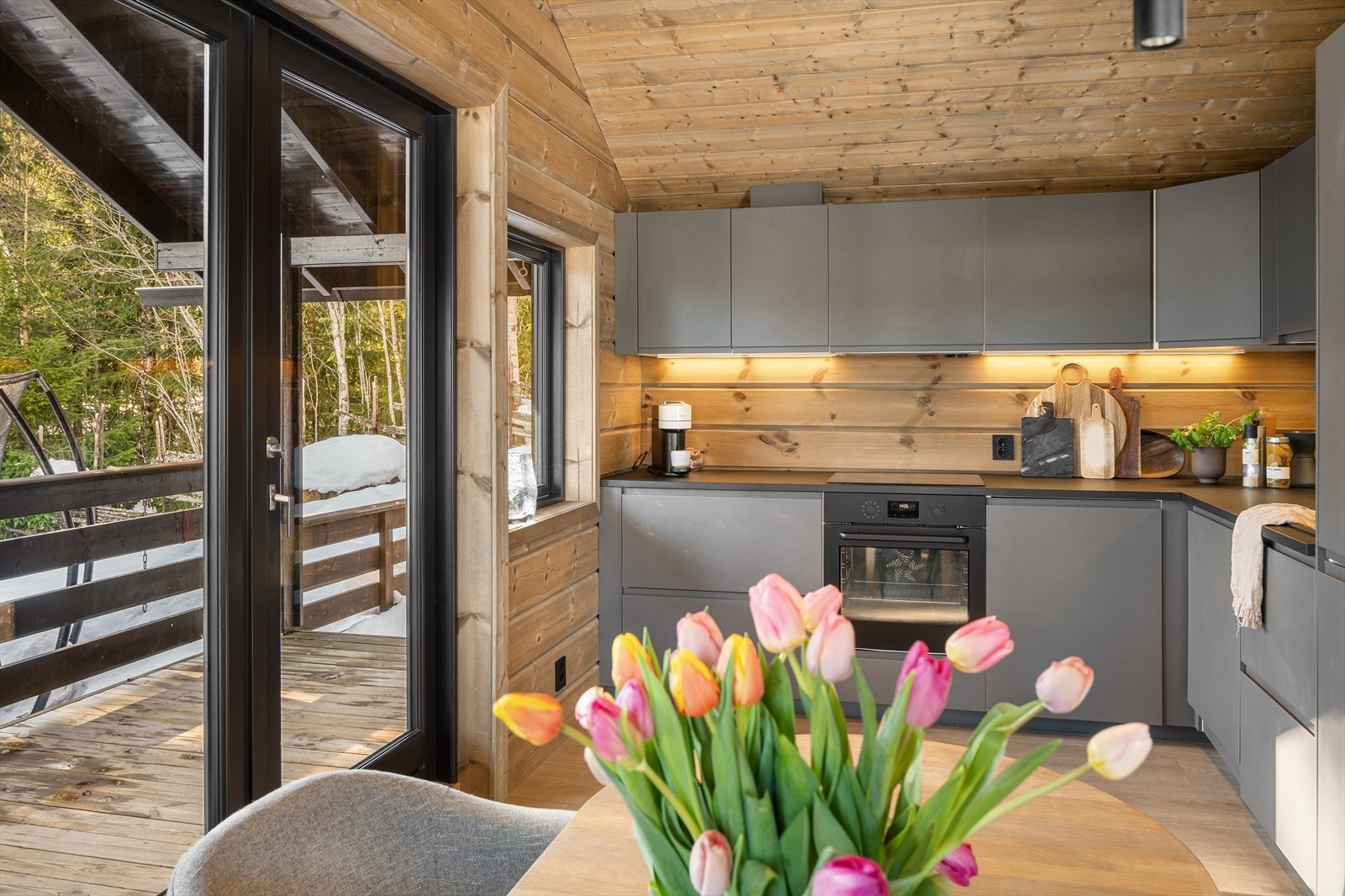 Kjøkkenet fremstår moderne og stilrent med slette, grå fronter som gir et tidløst og elegant uttrykk. Den praktiske laminatbenkeplaten gir gode arbeidsflater og tåler hyttelivets bruk godt, samtidig som den harmonerer fint med de rolige fargetonene. Galleribilde