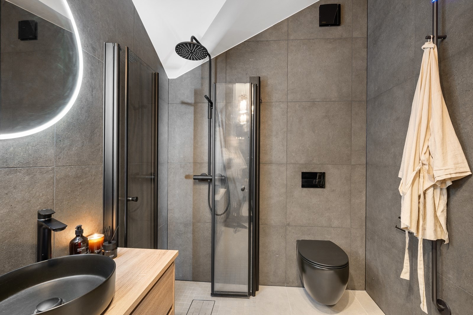 Den sorte vegghengte toalettløsningen, regnfallsdusj med sort armatur og sort servantskål på moderne skuffeinnredning skaper en helhetlig og elegant designlinje. Galleribilde