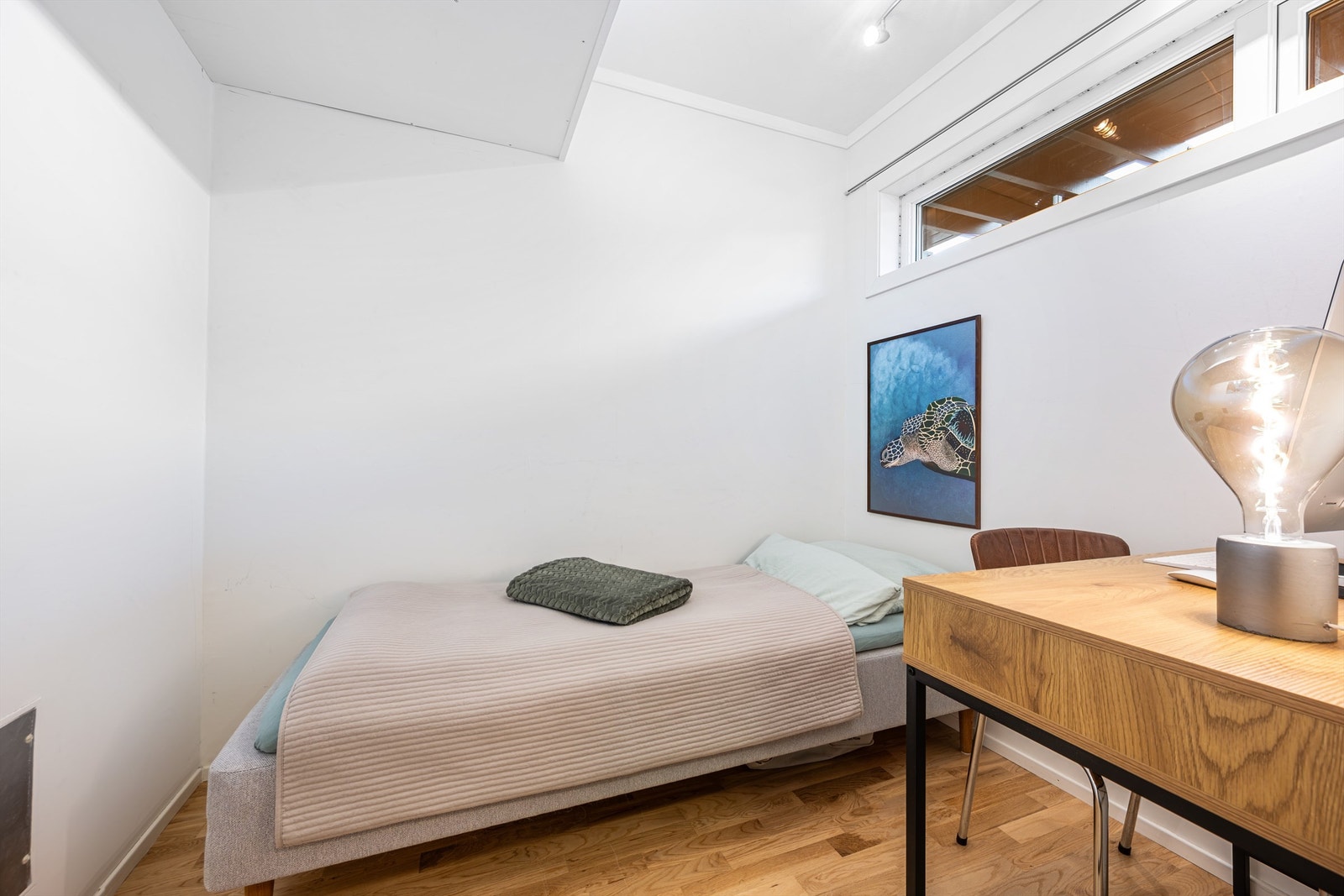 Innvendig bod har plass til både seng og kontor. Parkett på gulv og lyse veggflater og tak. Det er lite vindu som kan åpnes. Galleribilde