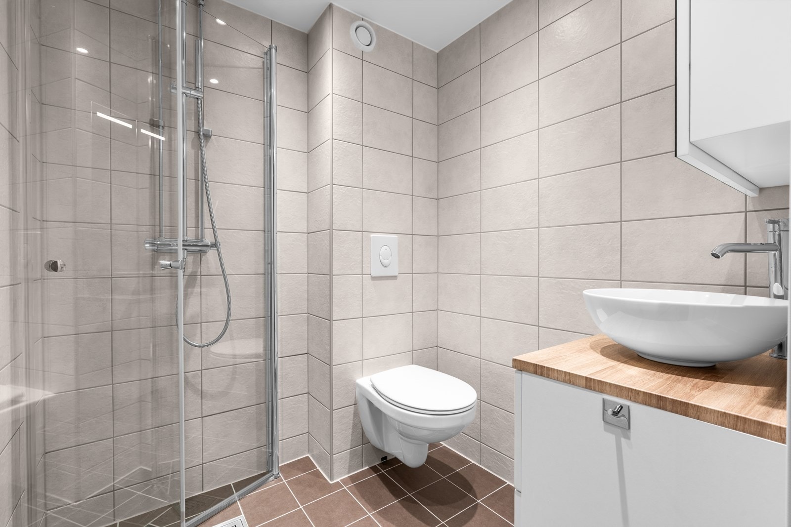 Badet er innredet med servantskap med ett-greps blandebatteri, speilskap, vegghengt toalett med innebygget sisterne, avskjermet dusjhjørne med glass, blandebatteri og dusjgarnityr. Galleribilde