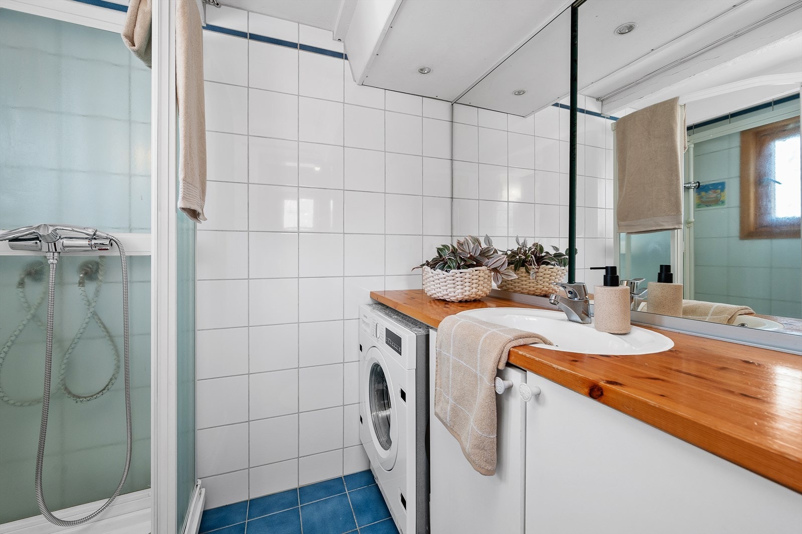 Badet i 1. etasje er innredet med fliser på gulv og vegger, dusjkabinett, servant med underskap og opplegg for vaskemaskin. Galleribilde