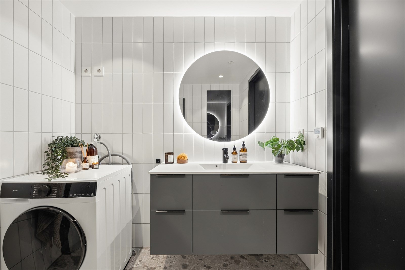 Badet er innredet med servantskap fra HTH, vegghengt speil med integrert lys over vask, vegghengt toalett, dusjsone med innfellbare glassdører og opplegg for vaskemaskin. Galleribilde