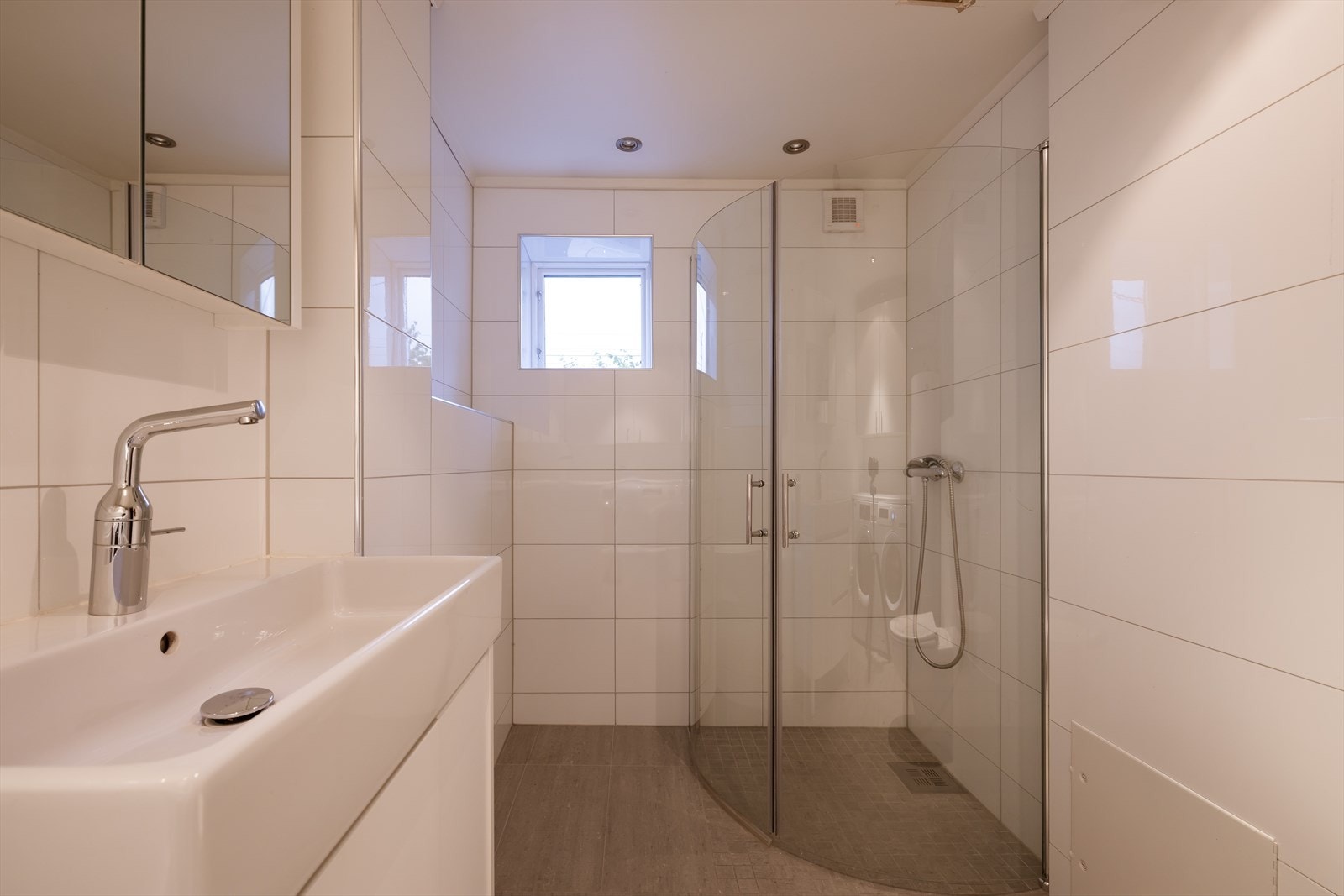 Baderommet har flislagte vegger og malt himling, med dusjhjørne med glassdører og vegghengt toalett. Galleribilde