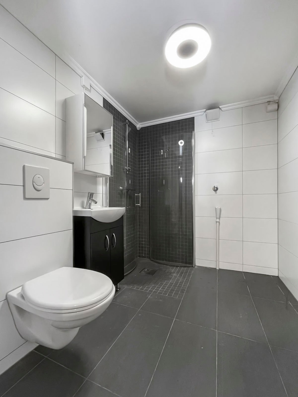 Baderom med flislagte vegger og flislagt gulv. Badet har dusjhjørne med glassdører og vegghengt toalett Galleribilde