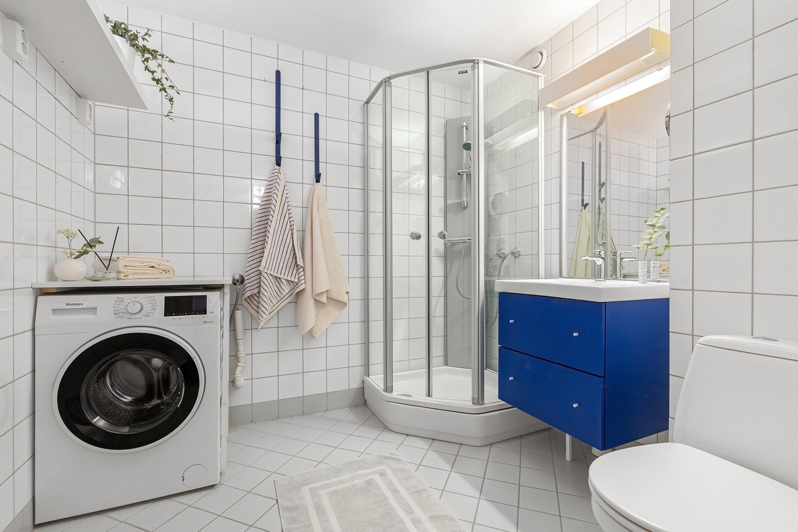 Leilighetens bad er helfliset og innredet med servant med underskap, dusjkabinett, opplegg for vaskemaskin og WC. Galleribilde