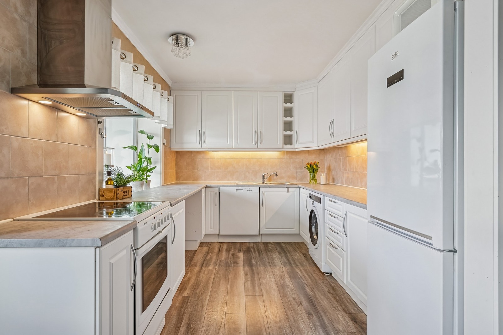 Lyst og pent kjøkken med god benkeplass, takhøye skap, oppvaskmaskin og vaskemaskin. Galleribilde