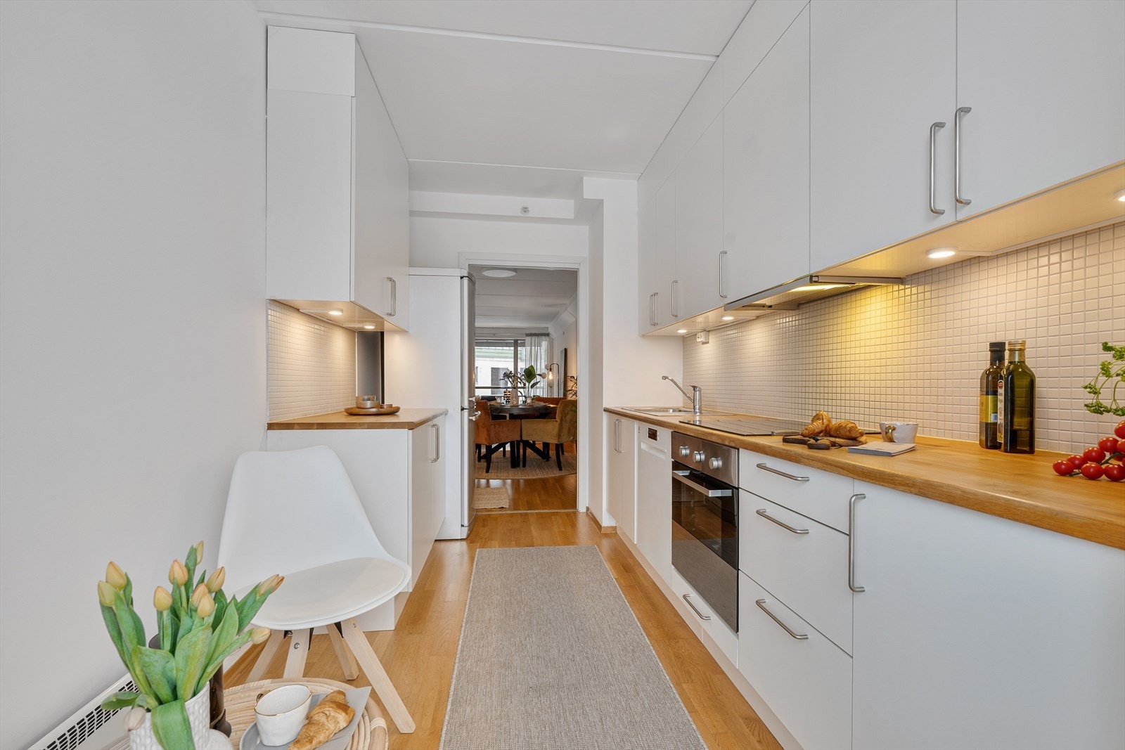 Lys og stilren kjøkkeninnredning fra Norema med integrerte hvitevarer bestående av platetopp, stekeovn og oppvaskmaskin. Galleribilde