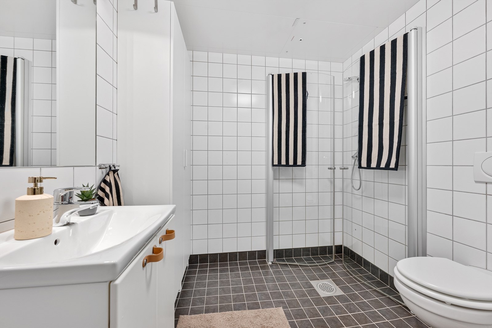 Videre er badet utstyrt med vegghengt toalett og dusjhjørne med svingbare dører. Galleribilde