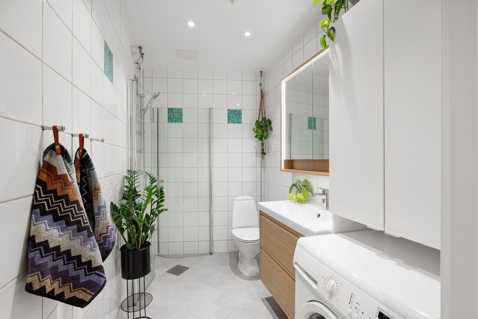 Pent og tidløst bad med lyse flater, elegant dusjhjørne og integrert opplegg for vaskemaskin. Galleribilde