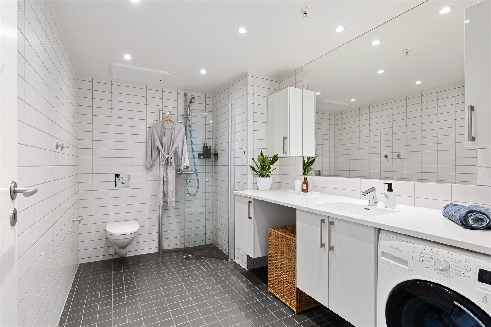 Pent og moderne, flislagt baderom med gulvvarme og downlights i himlingen. Badet er innredet med benkeplate med servantskap og nedfelt servant, innmurt speil samt praktisk veggskap for ekstra oppbevaring. Galleribilde