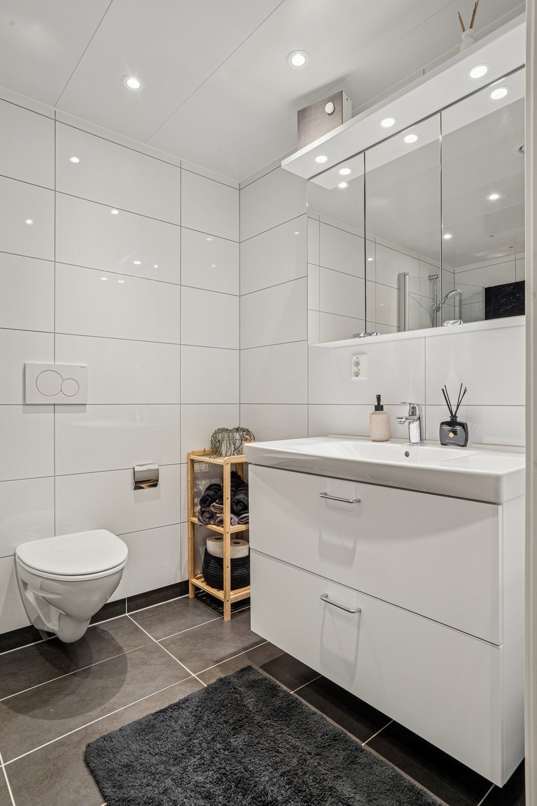 Rommet er innredet med servant nedfelt i baderomsinnredning, veggmontert toalett og et dusjhjørne med dusjvegger. Galleribilde