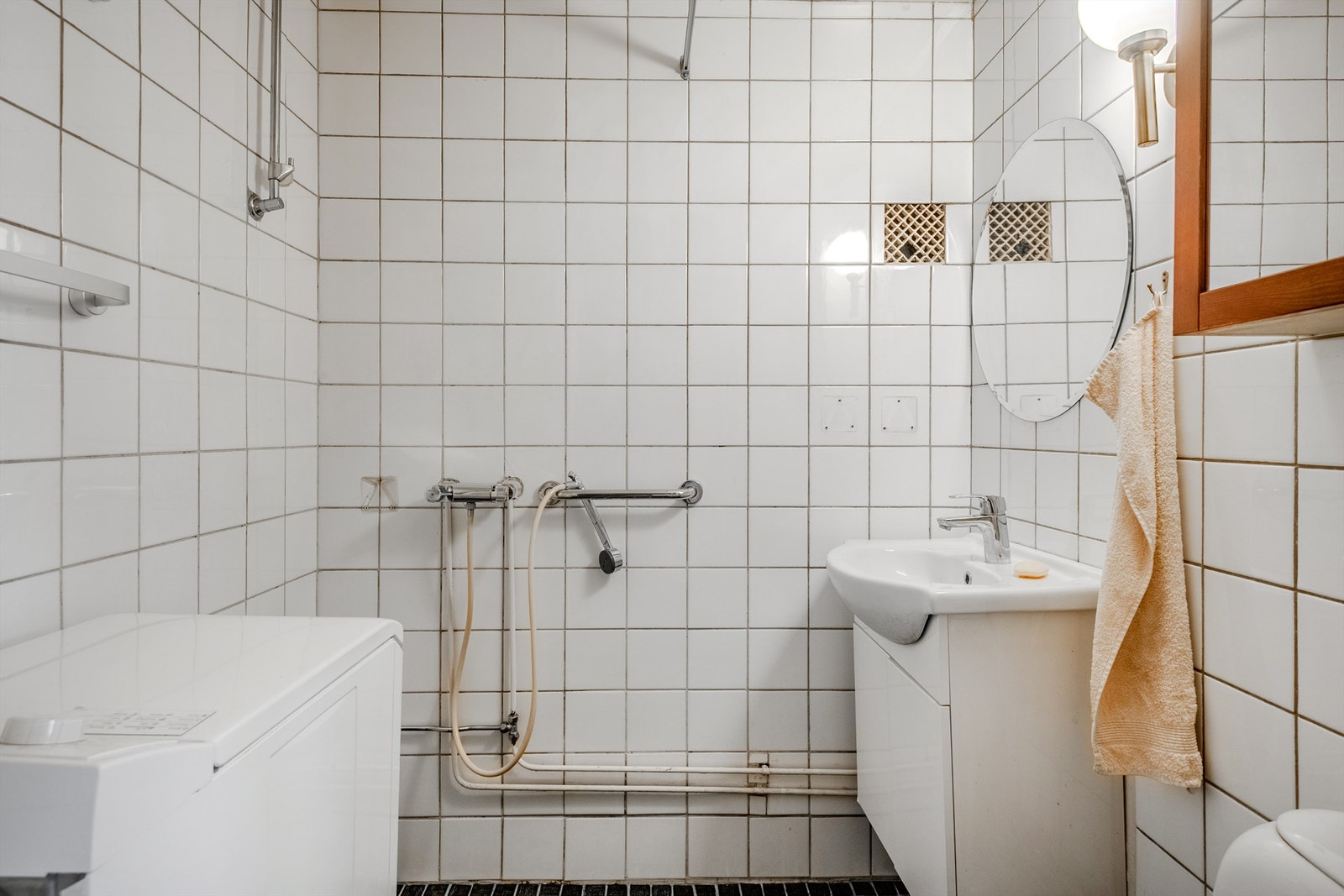 Flislagt baderom innredet med dusj, servant med skap, WC og opplegg for vaskemaskin. Galleribilde